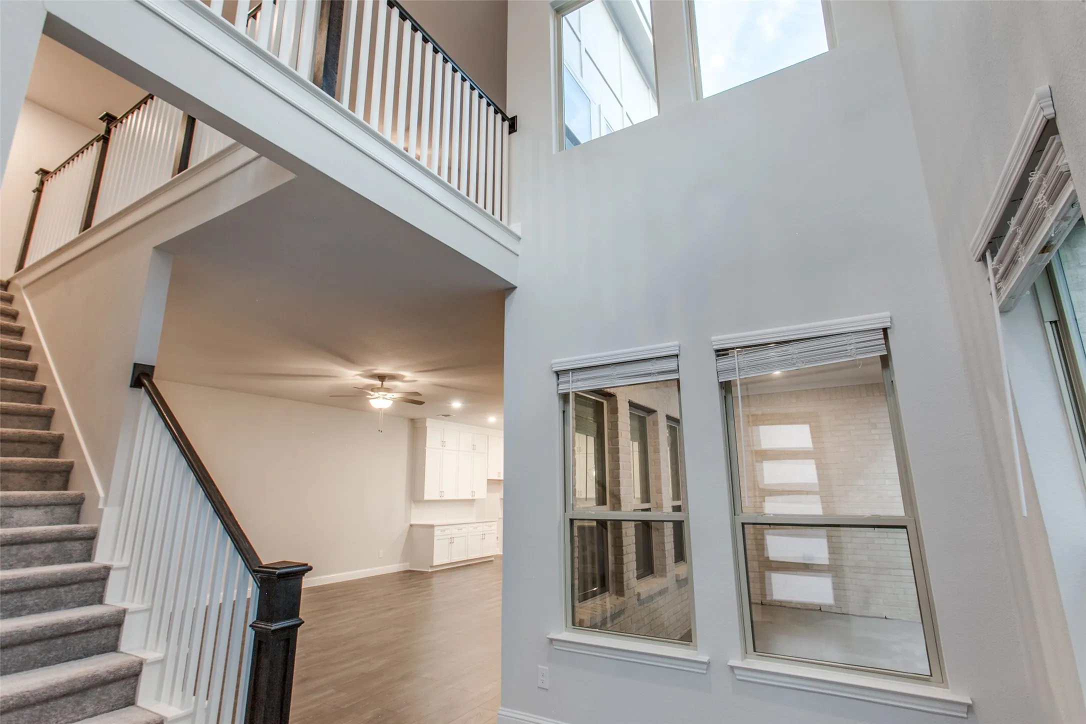 Two-story foyer featuring a carpeted staircase with white risers and dark wood handrails, a second-story landing with matching railings, tall windows with blinds, and white walls