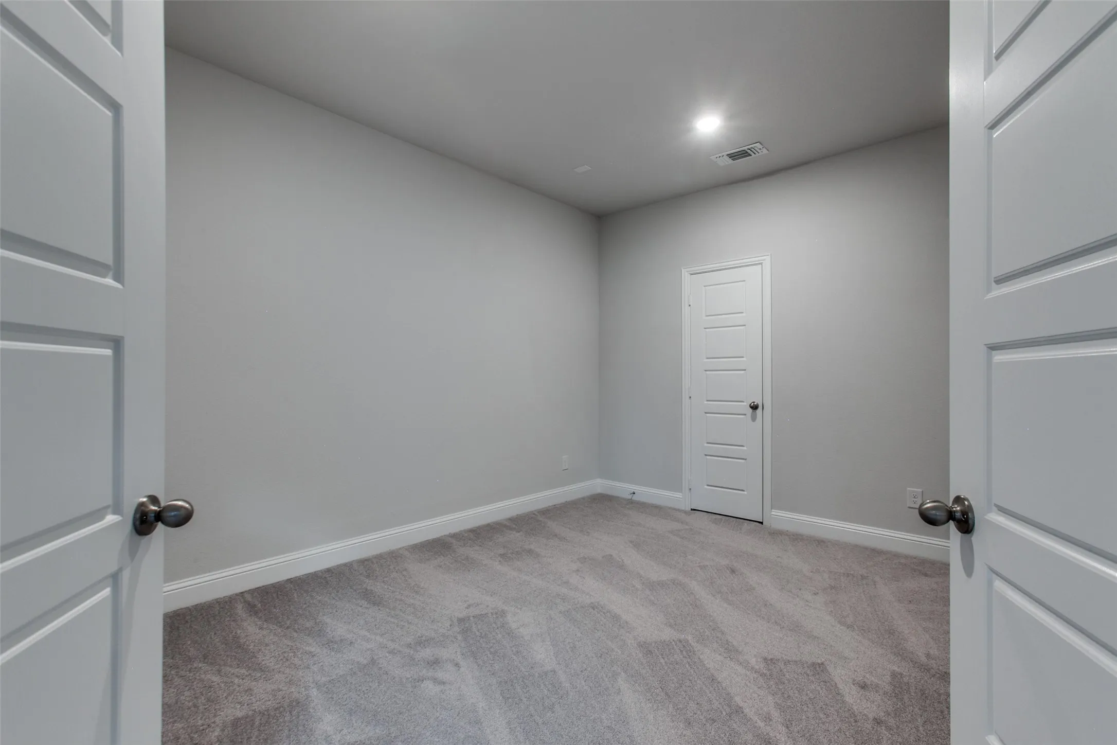 Gray carpeted room featuring light gray walls, white baseboards, and white paneled doors with dark hardware