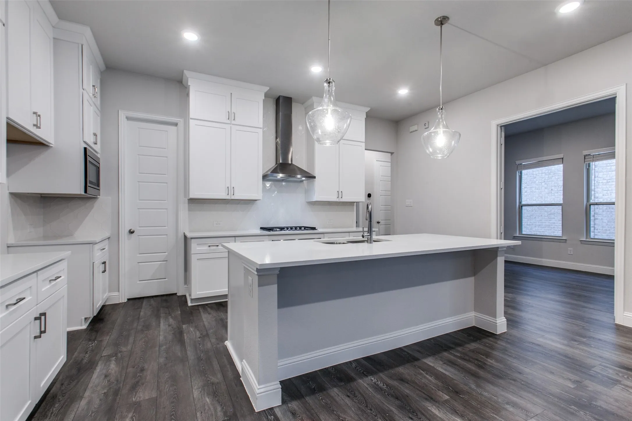 Kitchen featuring a central island with a sink, white cabinetry, integrated microwave, stainless steel range hood, and wood-finish flooring