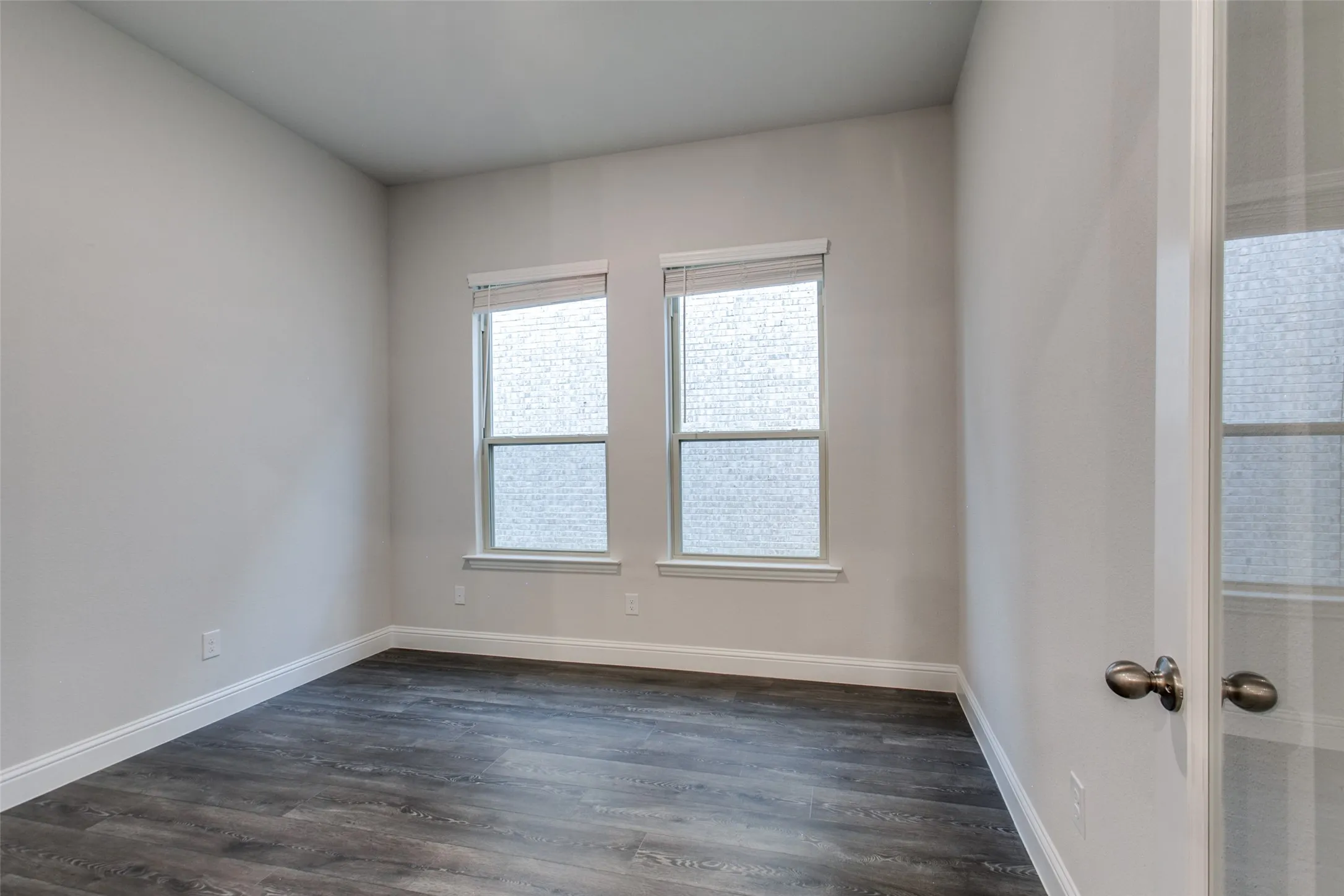 Room featuring two windows with privacy blinds, wood-finish flooring, and white baseboards