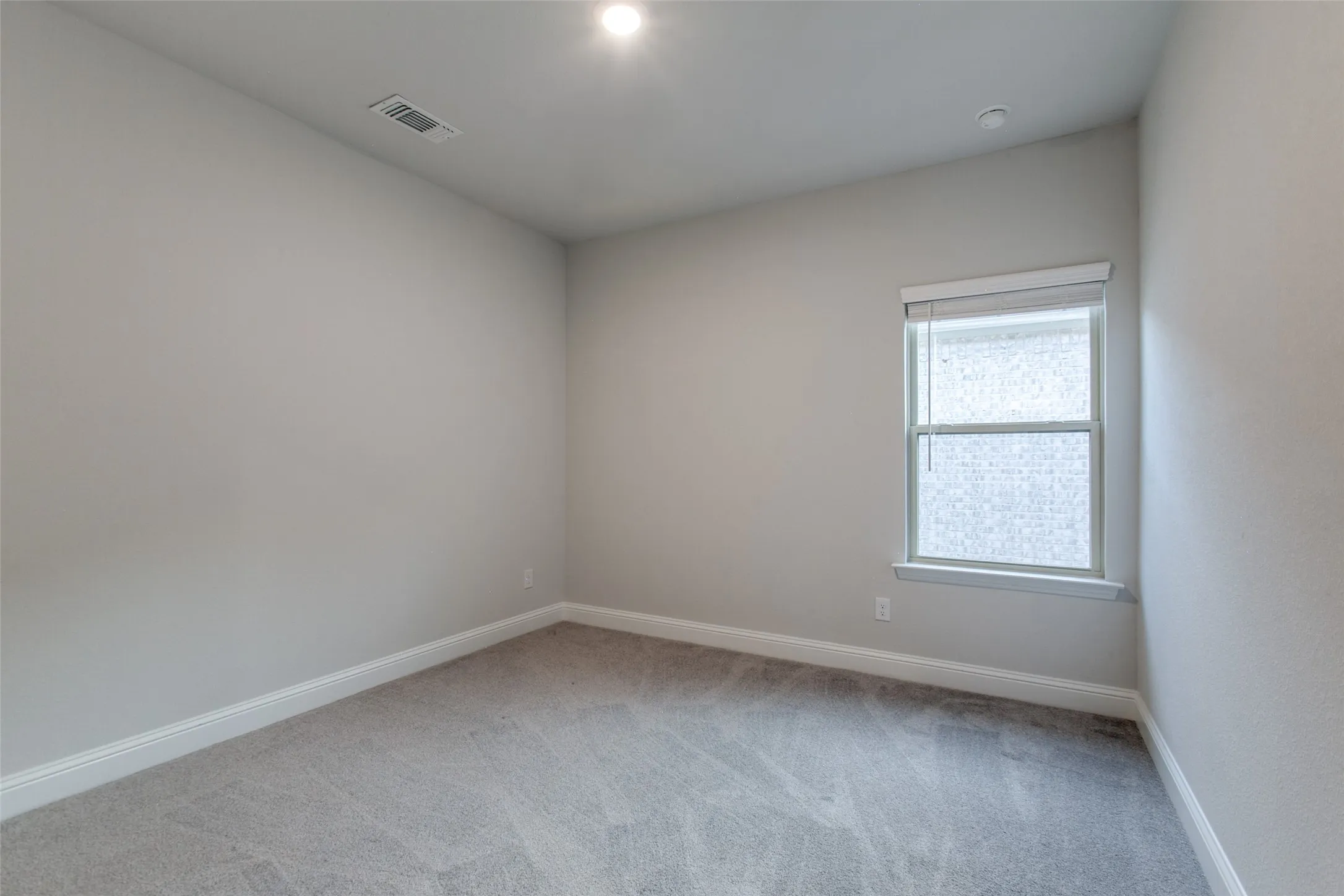 Neutral-toned room featuring a single window with blinds, recessed ceiling lighting, and carpet flooring