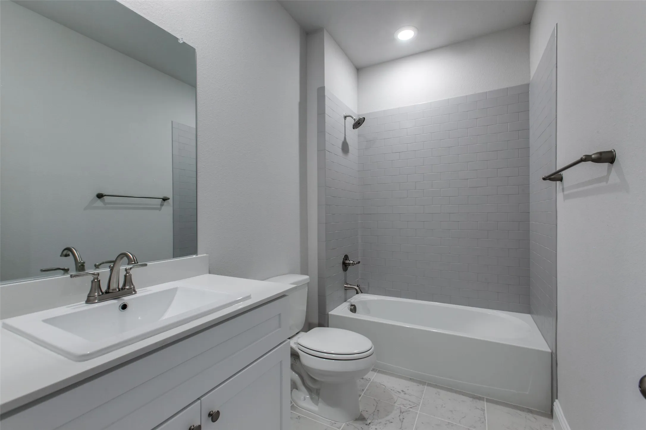 Full bathroom featuring a white vanity with integrated sink, brushed nickel faucet, frameless mirror, white toilet, and a combined tub/shower with subway tile surround