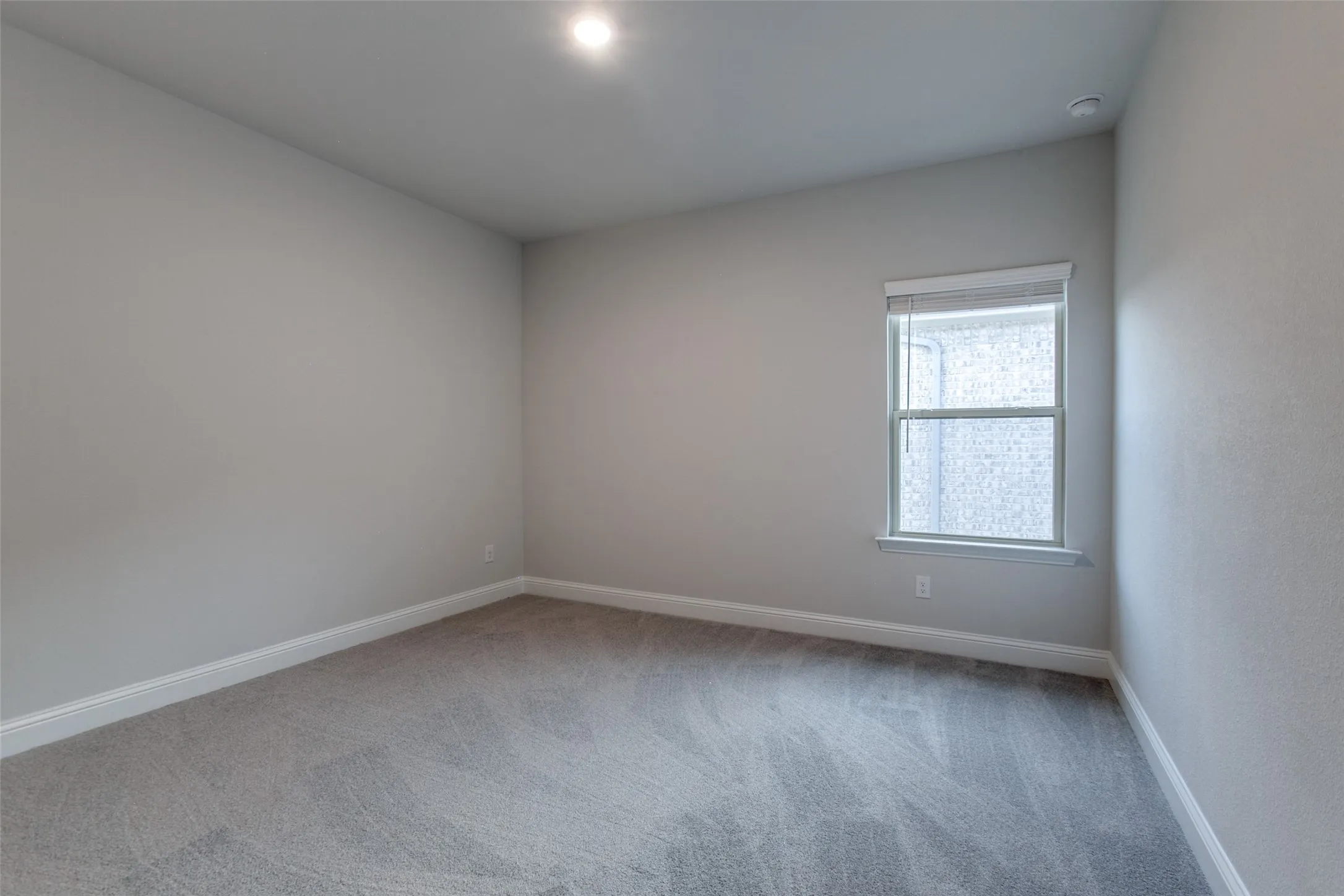 Light gray carpeted room featuring a single window with blinds and recessed ceiling lighting