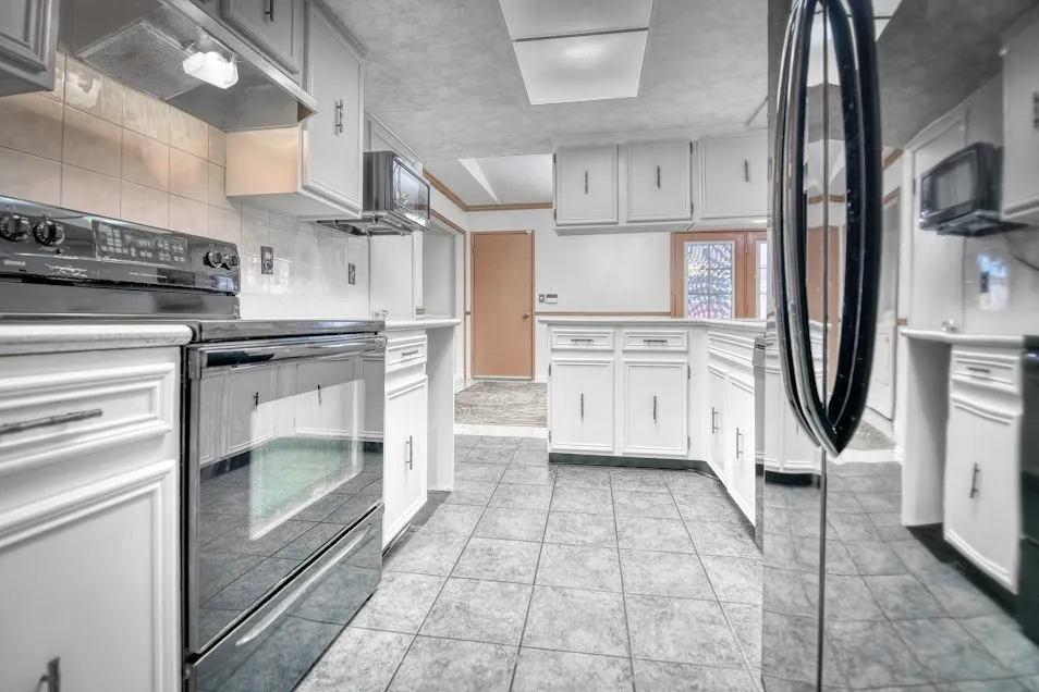 Kitchen featuring white cabinetry, tile flooring, black range, black microwave, and a window with decorative glass