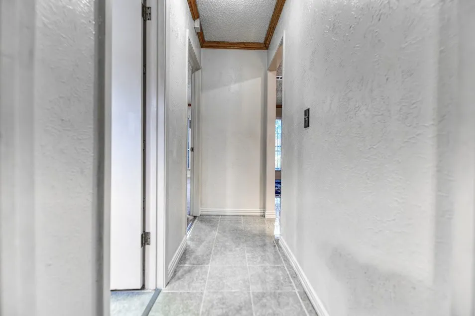 Hallway featuring textured white walls, light gray tile flooring, white trim, and a wood-finish ceiling accent