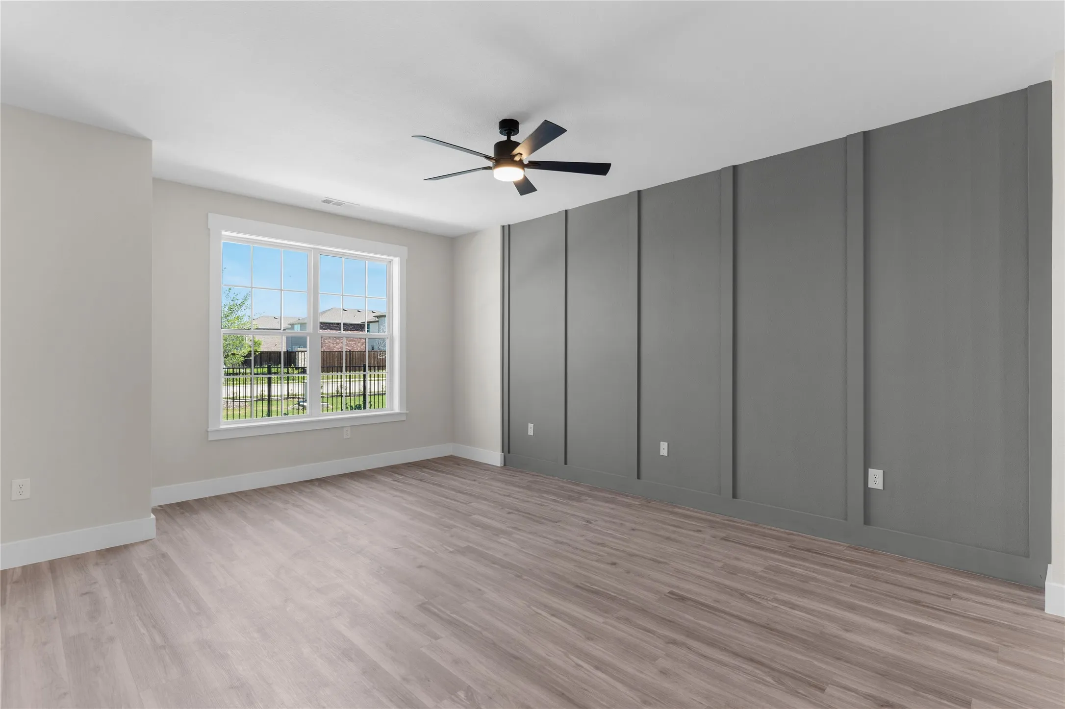 Spacious room featuring wood-finish flooring, a contemporary ceiling fan with integrated lighting, and a prominent accent wall with vertical paneling