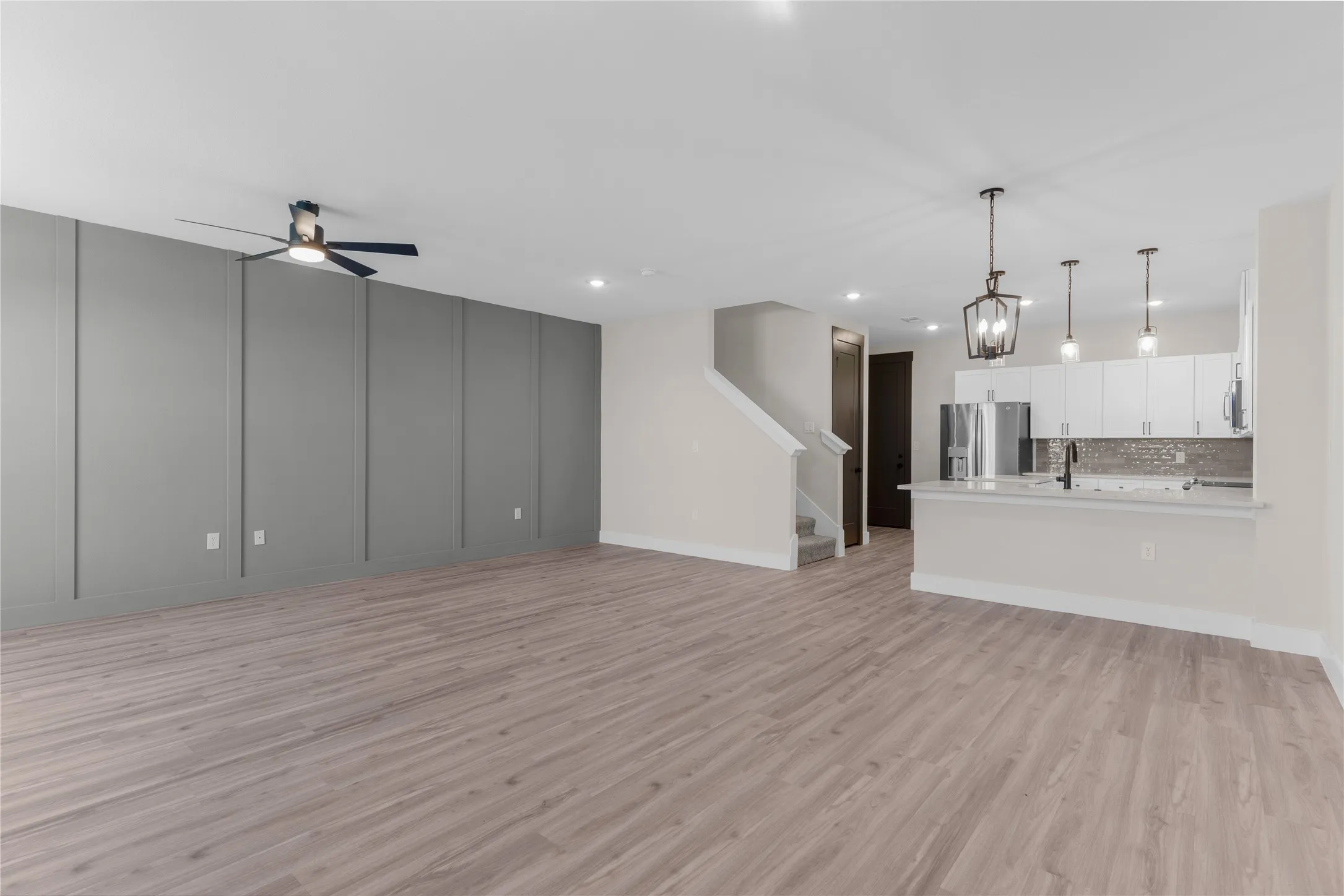 Spacious open-concept living area featuring wood-finish flooring, a contemporary accent wall, and a ceiling fan
