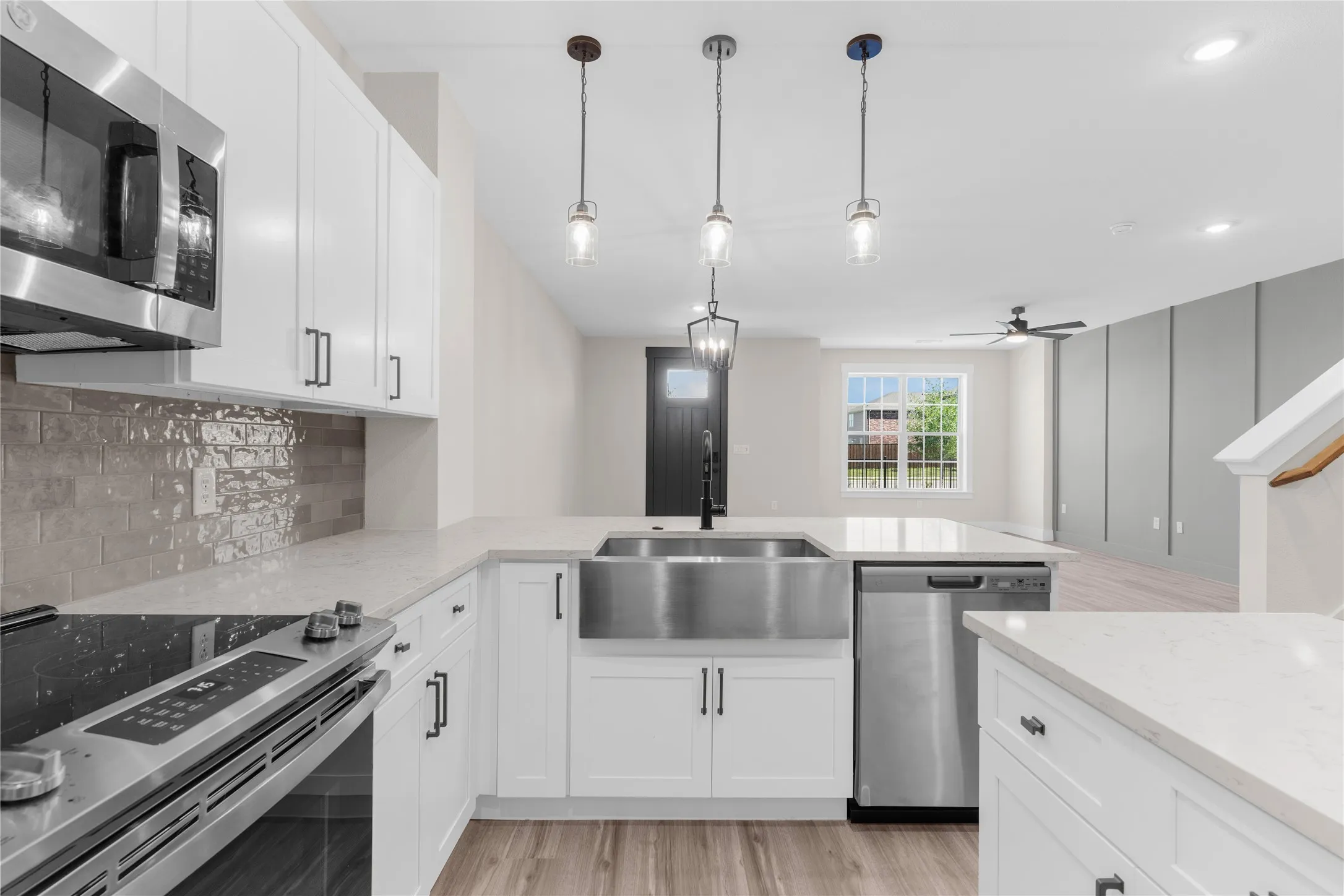 Modern kitchen with white cabinetry and light countertops, featuring stainless steel appliances, a farmhouse sink, and contemporary pendant lighting