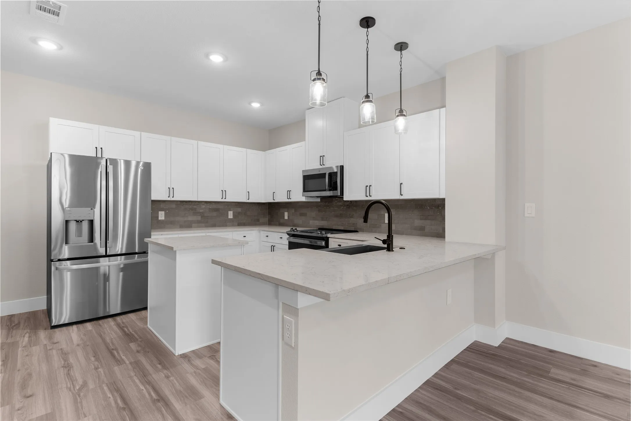 Modern kitchen featuring white cabinetry, light-toned countertops, stainless steel appliances, and wood-finish flooring