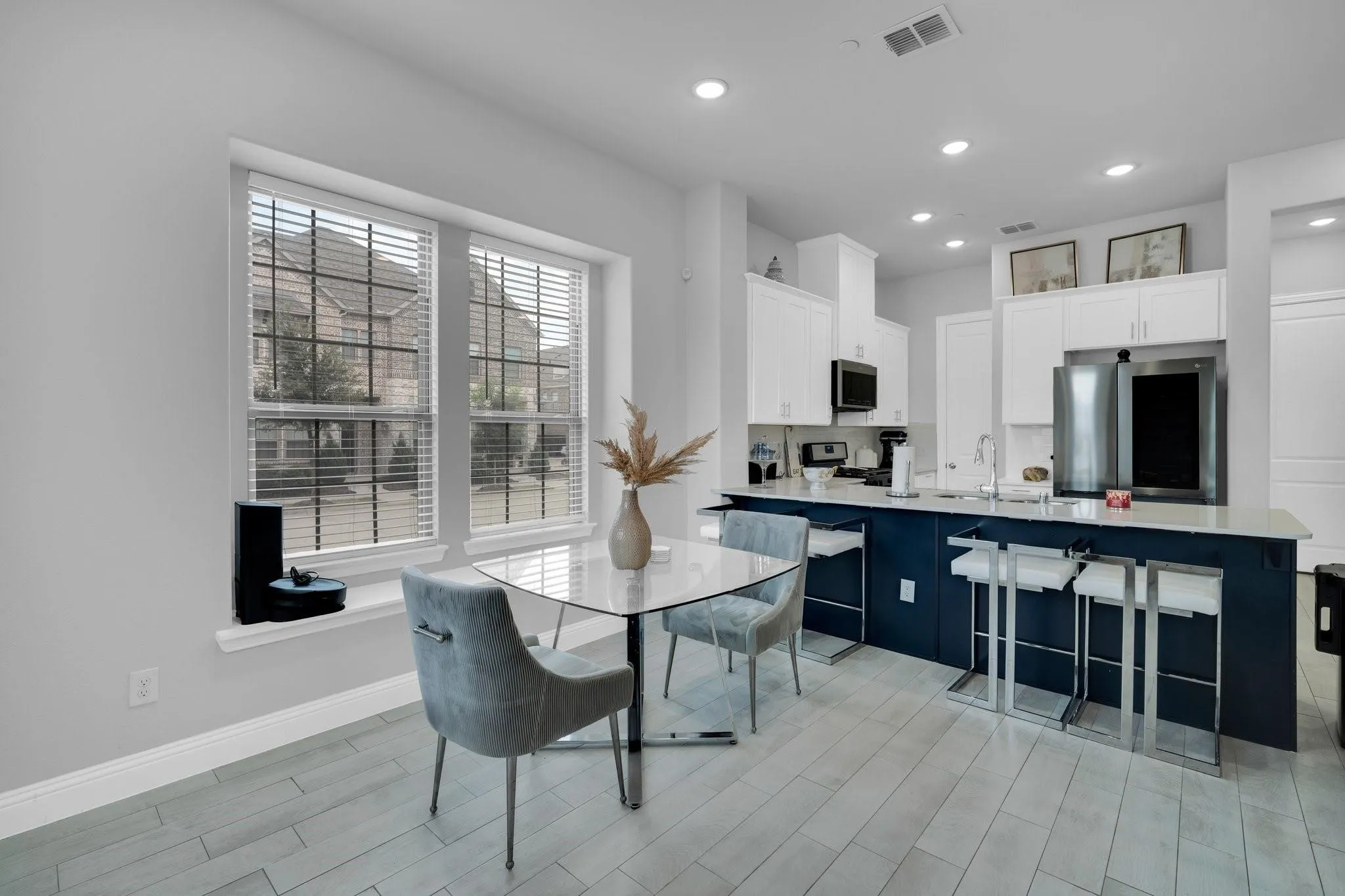 Contemporary kitchen featuring a large central island with seating, white shaker cabinetry, stainless steel appliances, and light wood-finish flooring