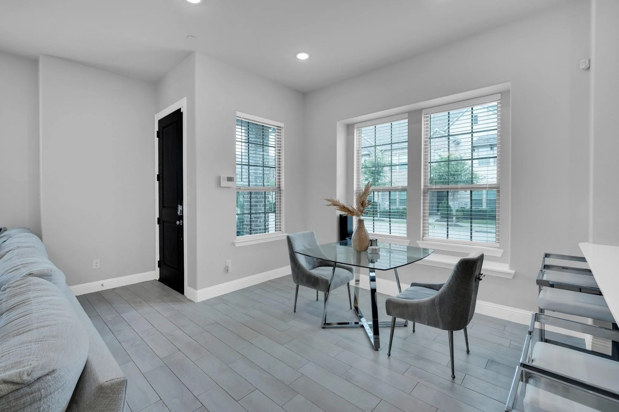 Living space featuring plank-style wood-finish flooring, two large windows with blinds, recessed lighting, and a dark paneled door with white trim