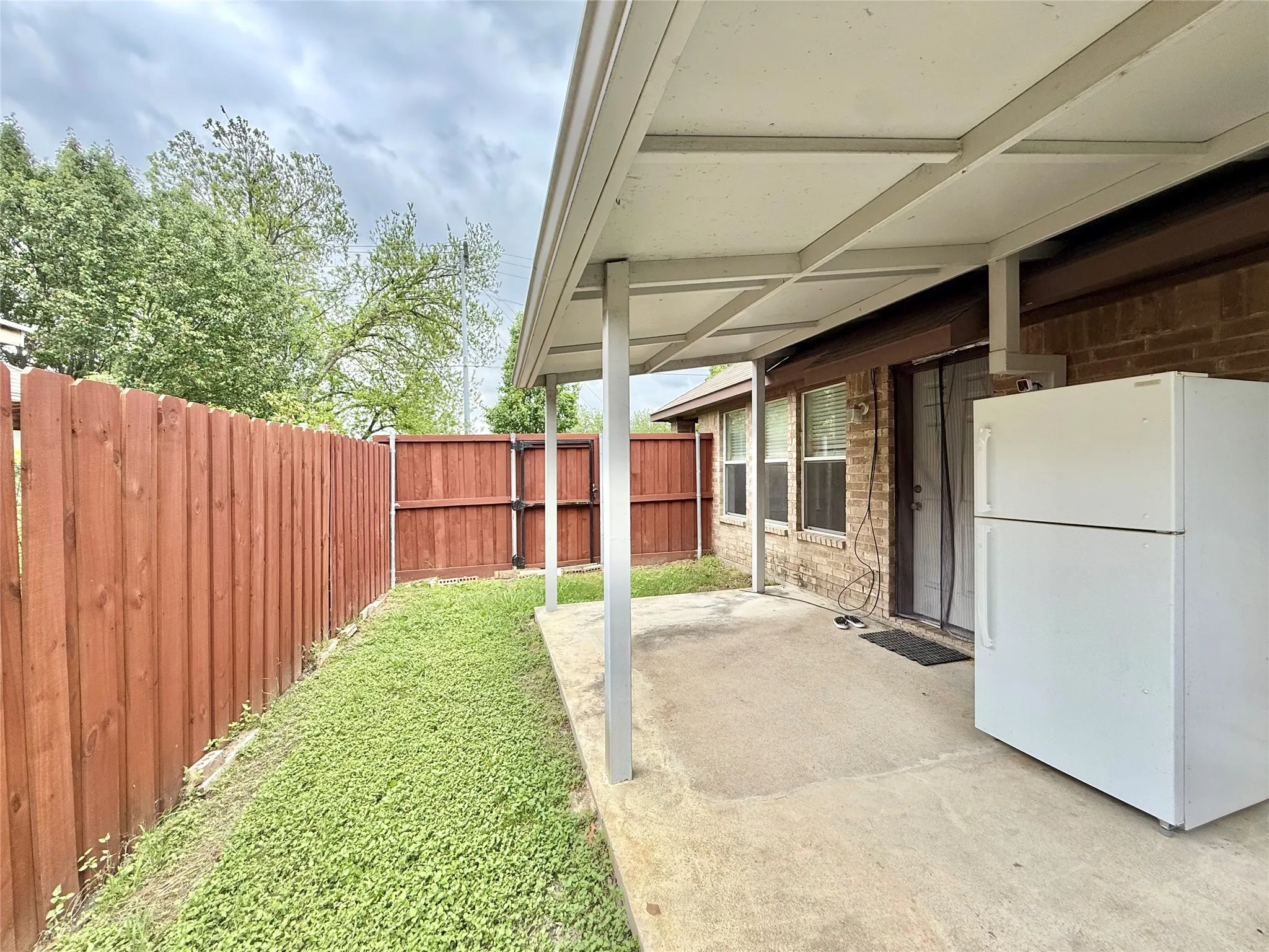 Concrete patio with an overhead cover, brick exterior, and a privacy fence
