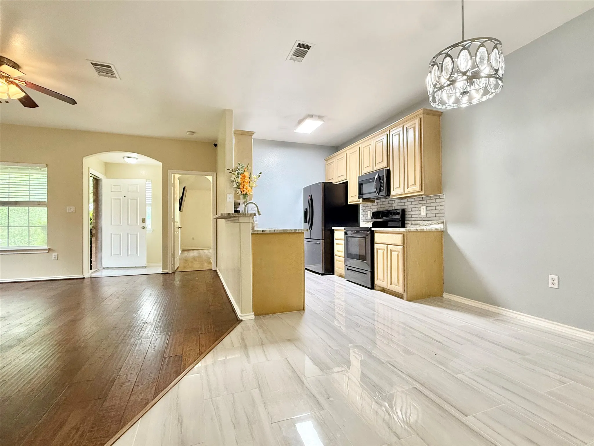 Kitchen with light wood cabinetry, black appliances, and a tiled backsplash