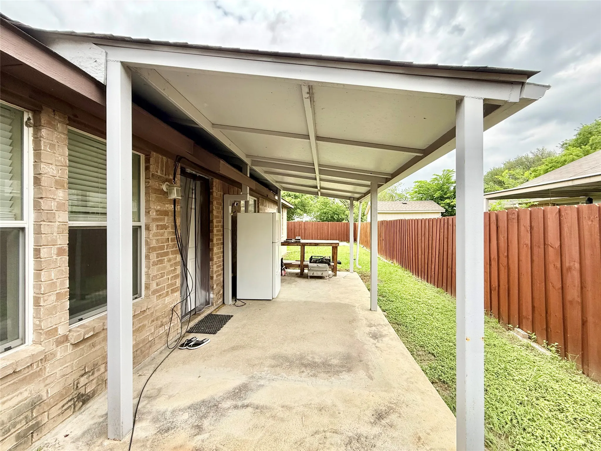 Covered concrete patio with a full privacy fence and a brick exterior
