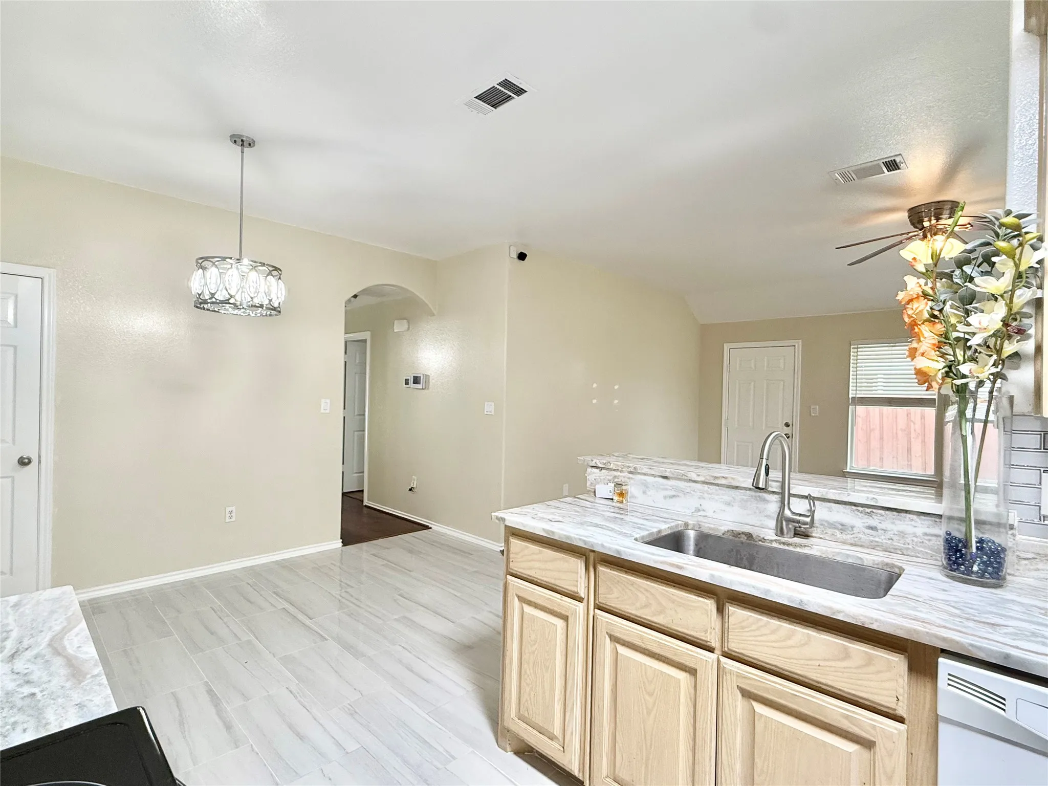 Kitchen area featuring light wood cabinetry, a stainless steel sink with a high-arc faucet, and light-toned countertop surfaces
