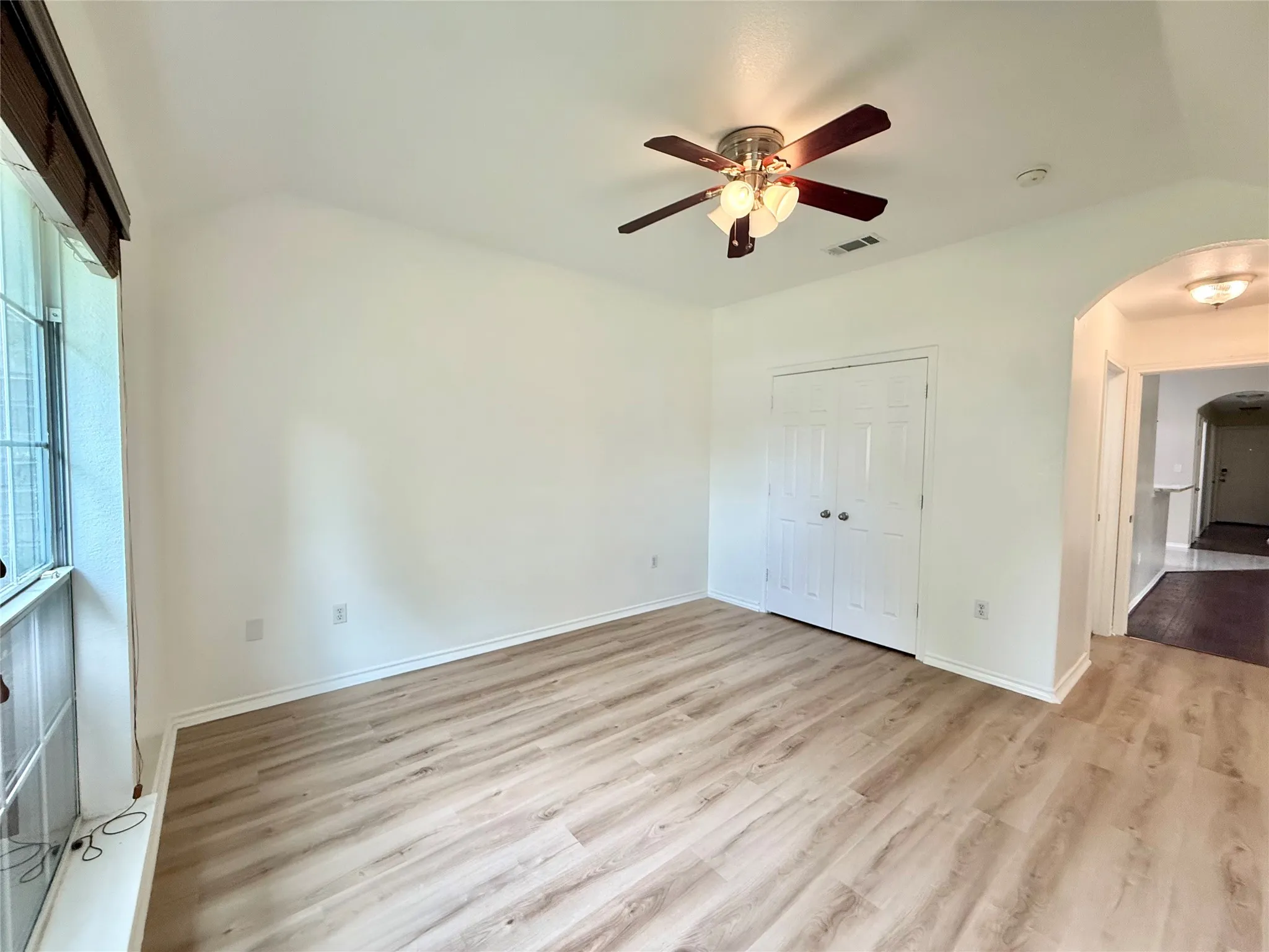 Room featuring vaulted ceilings, wood-finish flooring, a ceiling fan with light fixture, and a window with blinds