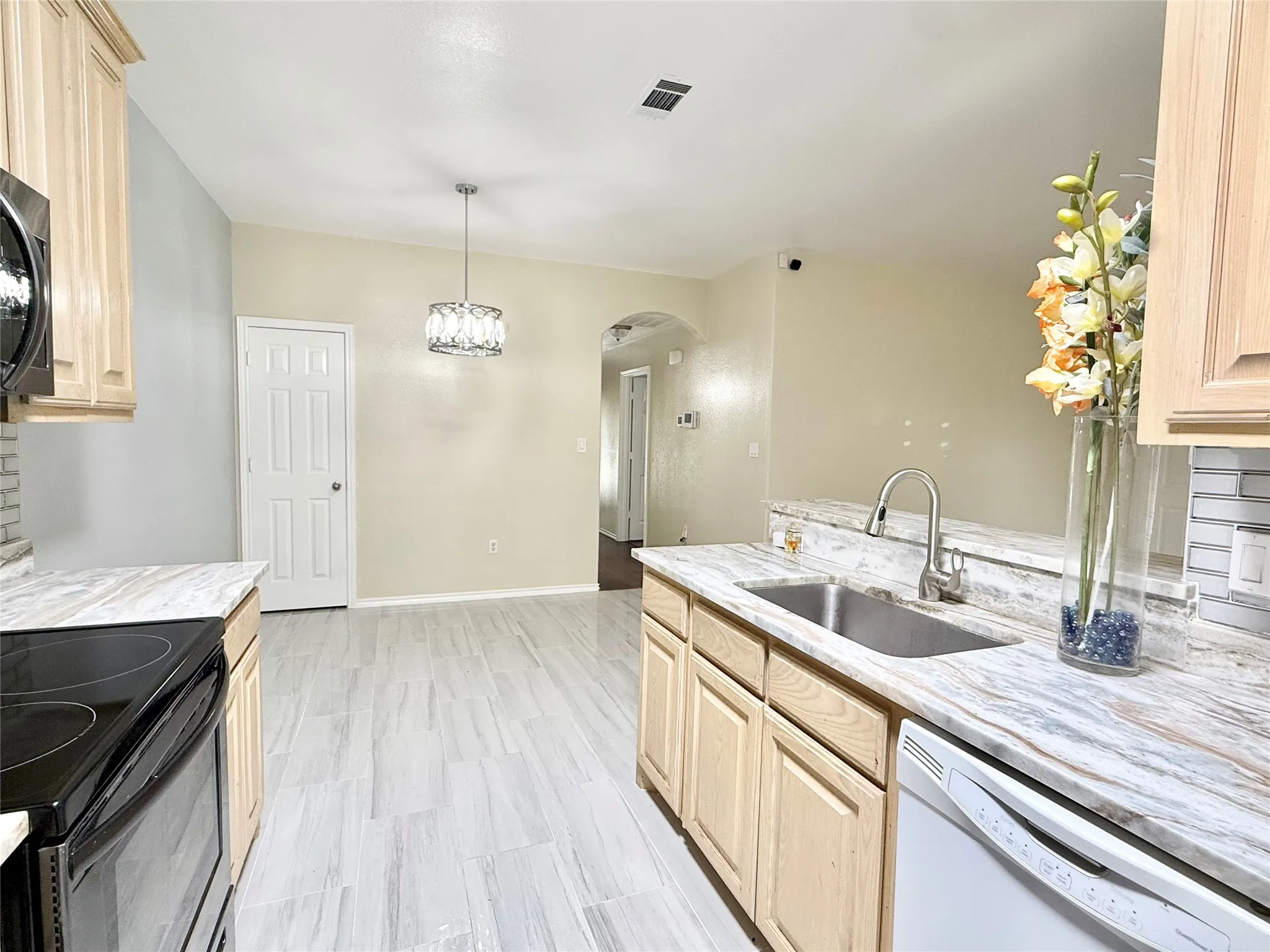 Kitchen featuring wood-finish cabinetry, stone countertops, stainless steel sink, and light-toned tile flooring