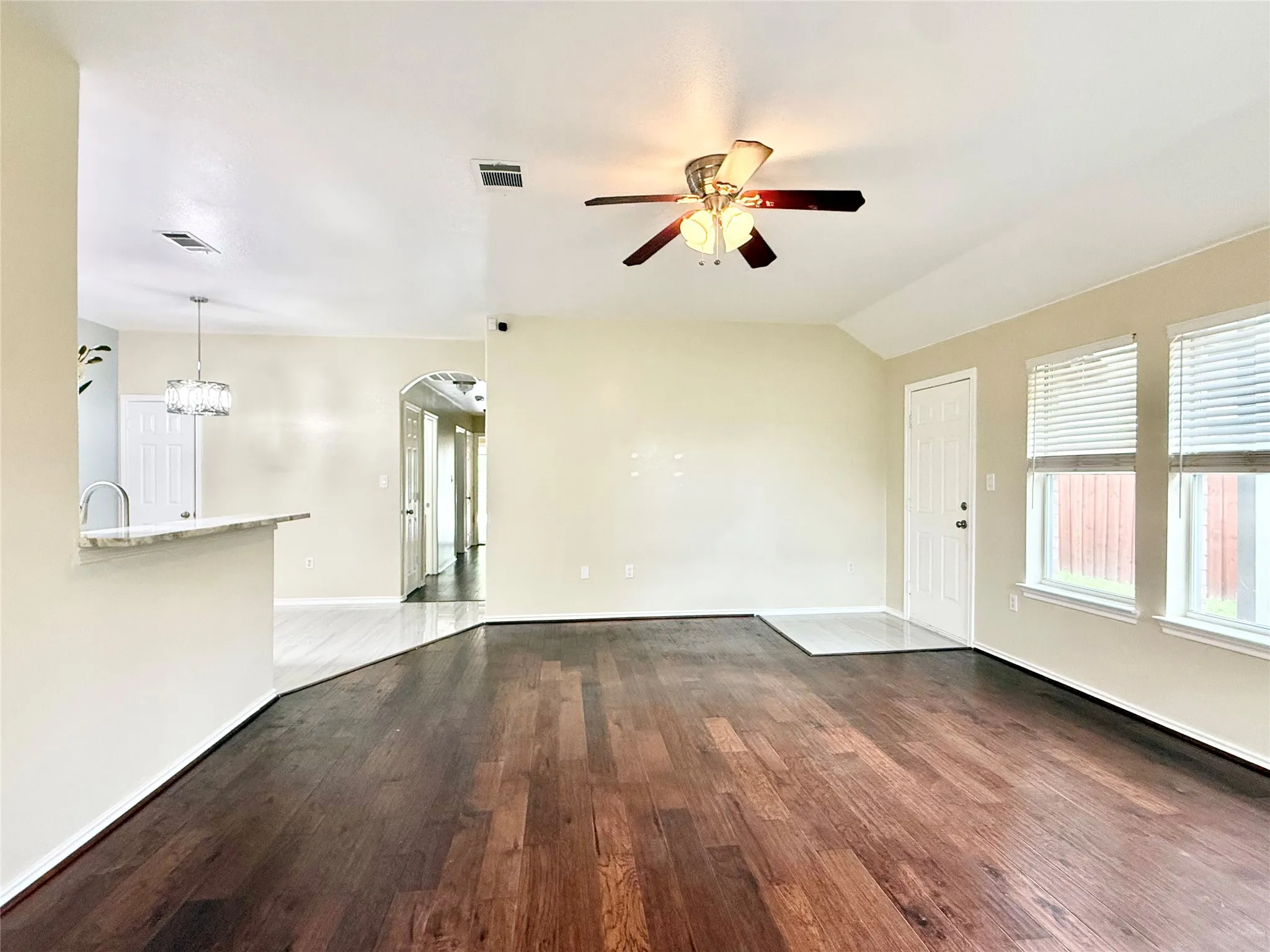 Spacious interior featuring rich wood-finish flooring, vaulted ceilings, and a modern ceiling fan with integrated lighting