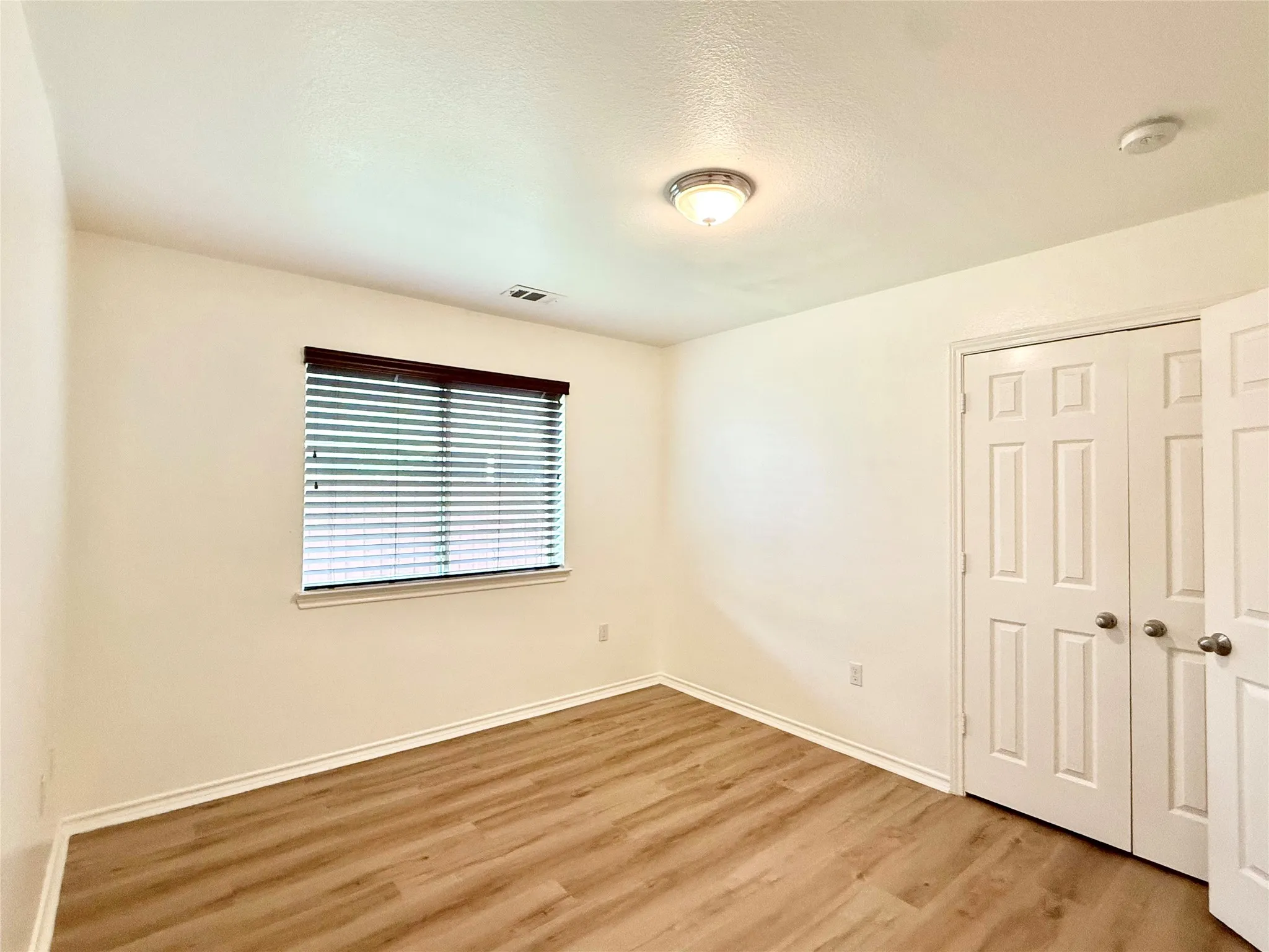 Bright interior space featuring wood-finish flooring, light-toned walls, and a window with blinds
