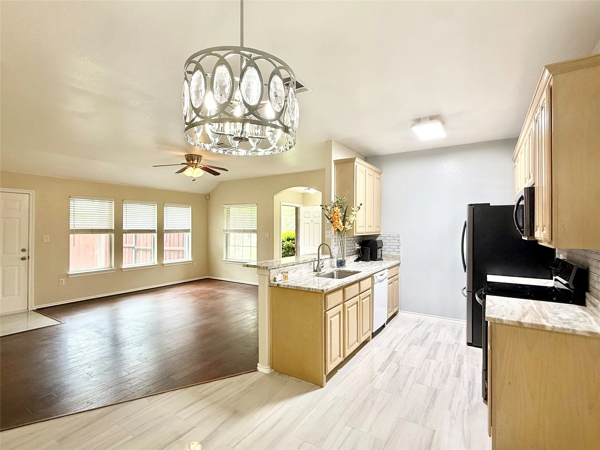 Open-concept kitchen featuring light wood cabinetry, stone-finish countertops, and a subway tile backsplash