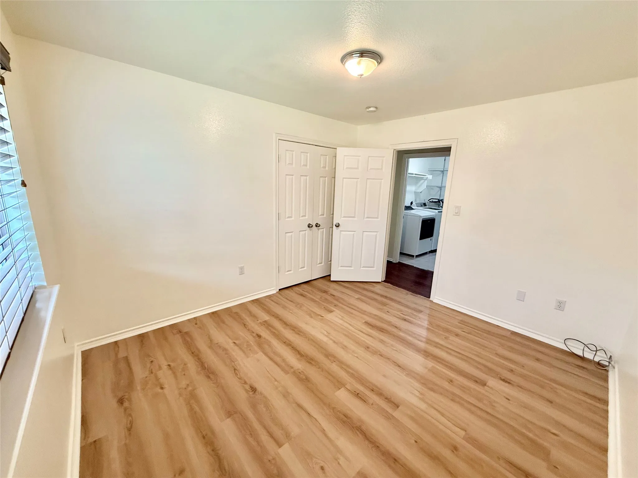 Spacious room featuring wood-finish flooring, white baseboards, and a window with horizontal blinds