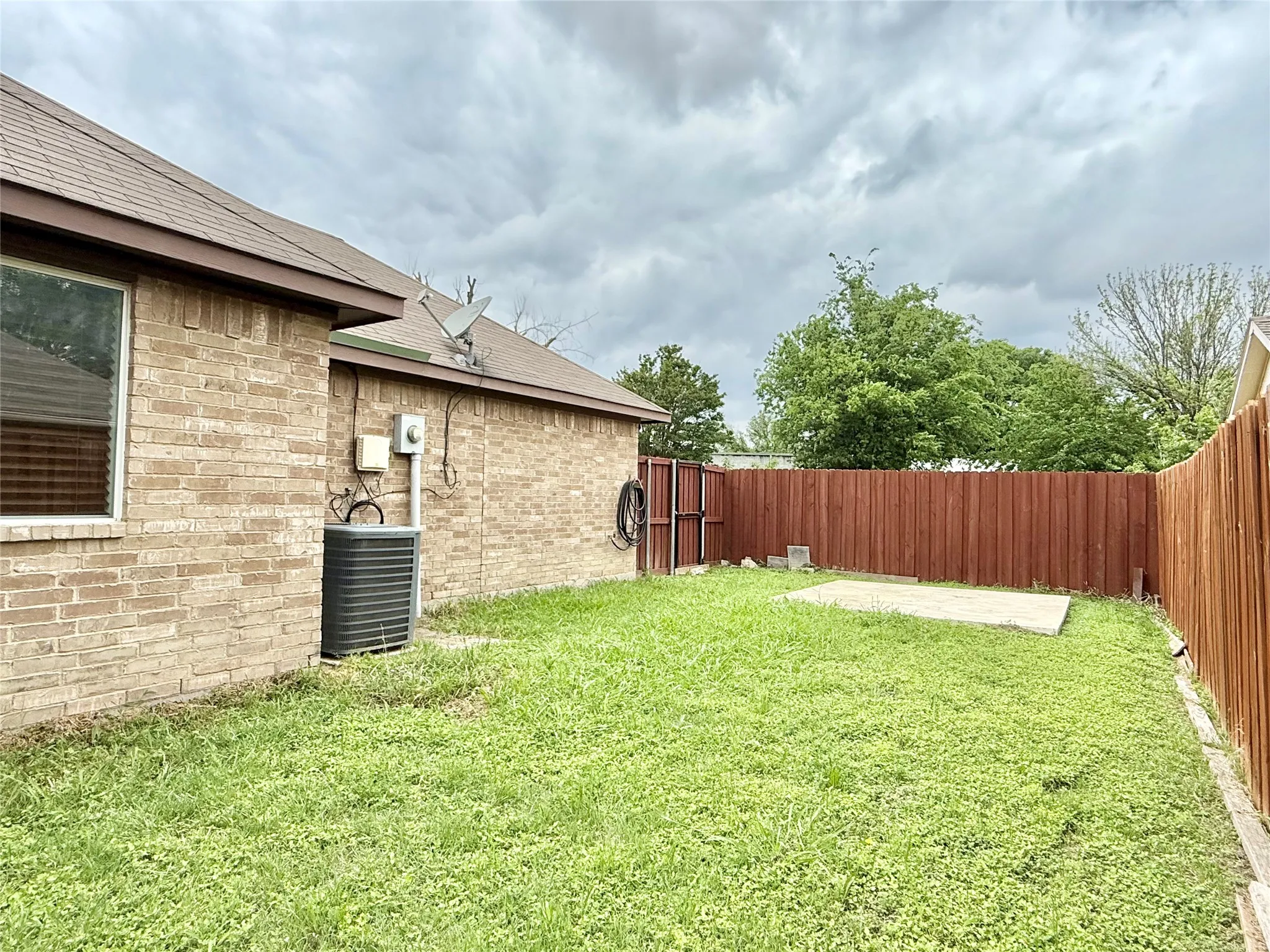 Spacious backyard featuring a brown privacy fence, a concrete patio slab, and a brick exterior home with a brown shingle roof