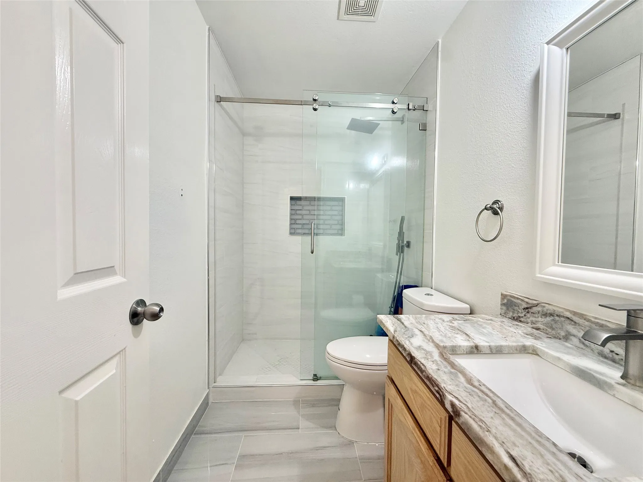 Bathroom featuring a glass-enclosed shower with subway tile, wood-finish vanity with stone countertop, undermount sink, and modern brushed nickel fixtures