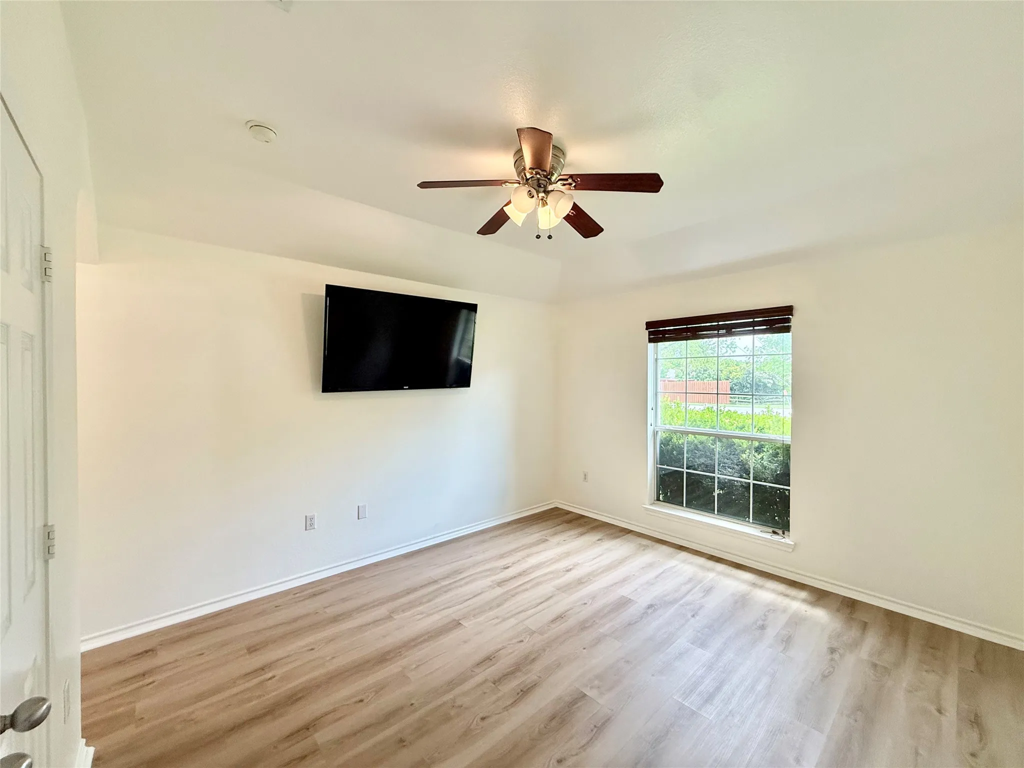 Bright interior space featuring wood-finish flooring, a contemporary ceiling fan with integrated lighting, and a double-pane window with dark wood-finish blinds