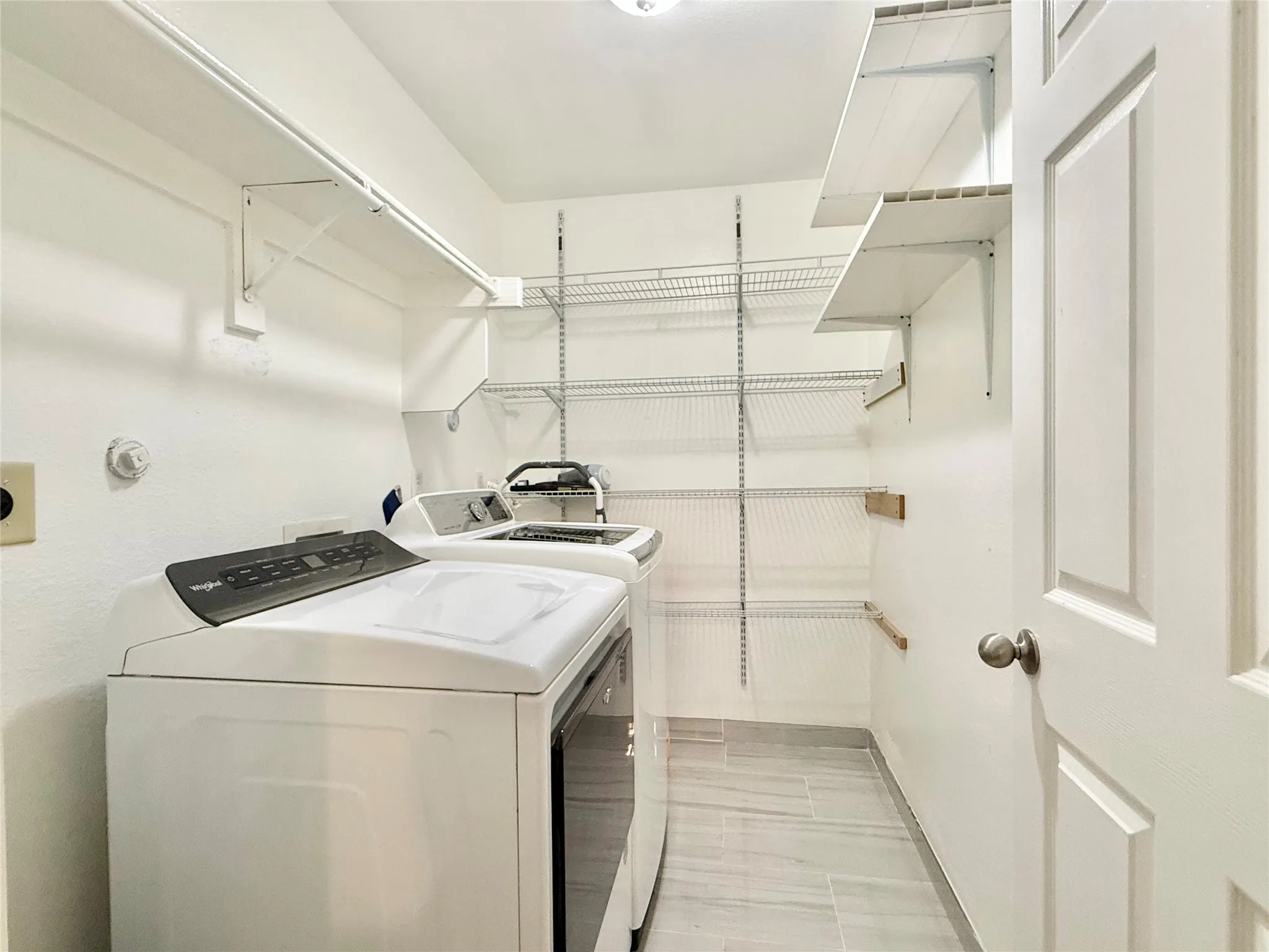 Dedicated laundry area featuring tile flooring, white walls, built-in wire shelving, and an overhead clothes rod