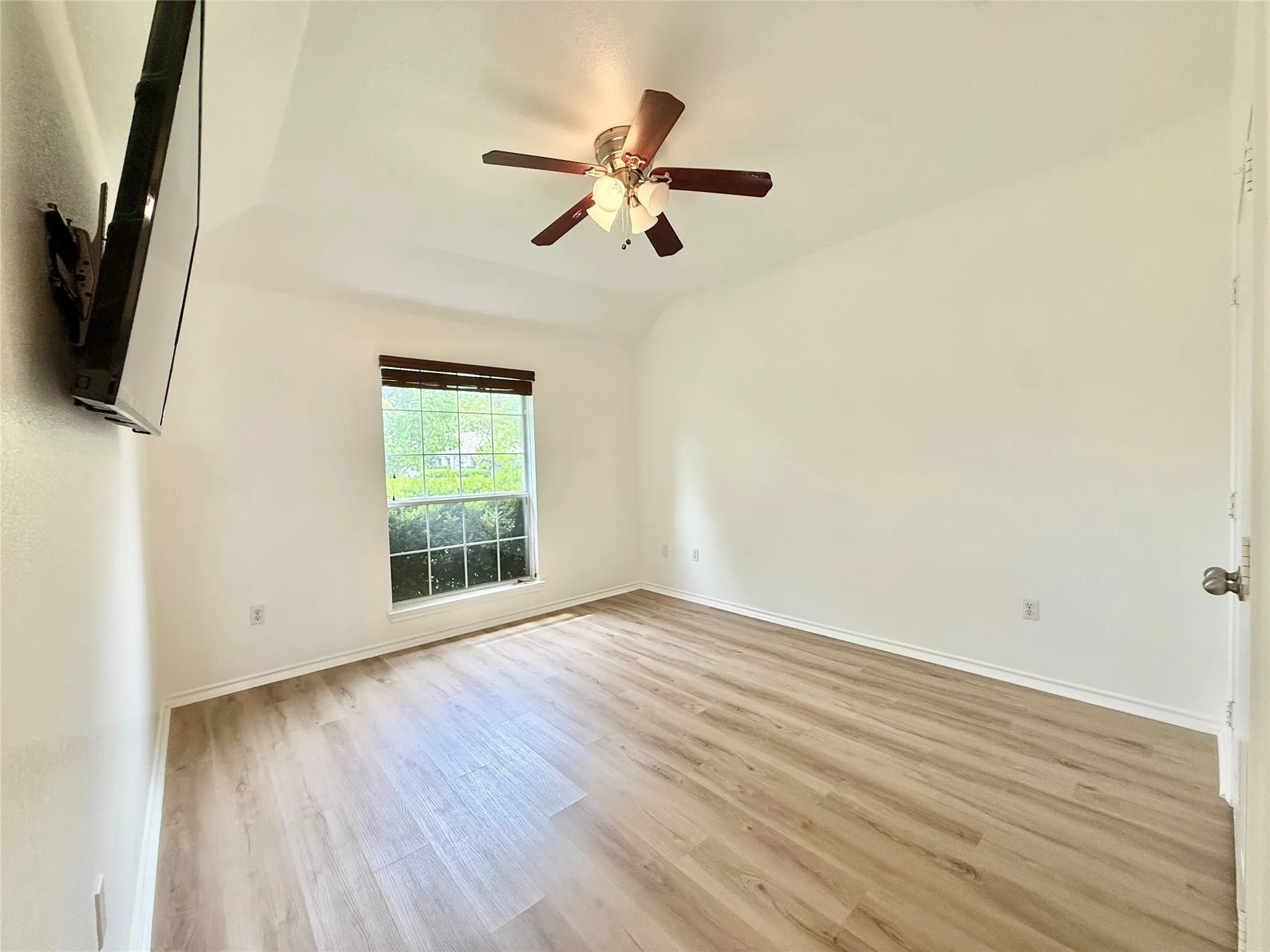 Bedroom with wood-finish flooring, a single window featuring horizontal blinds, and a ceiling fan with integrated lighting