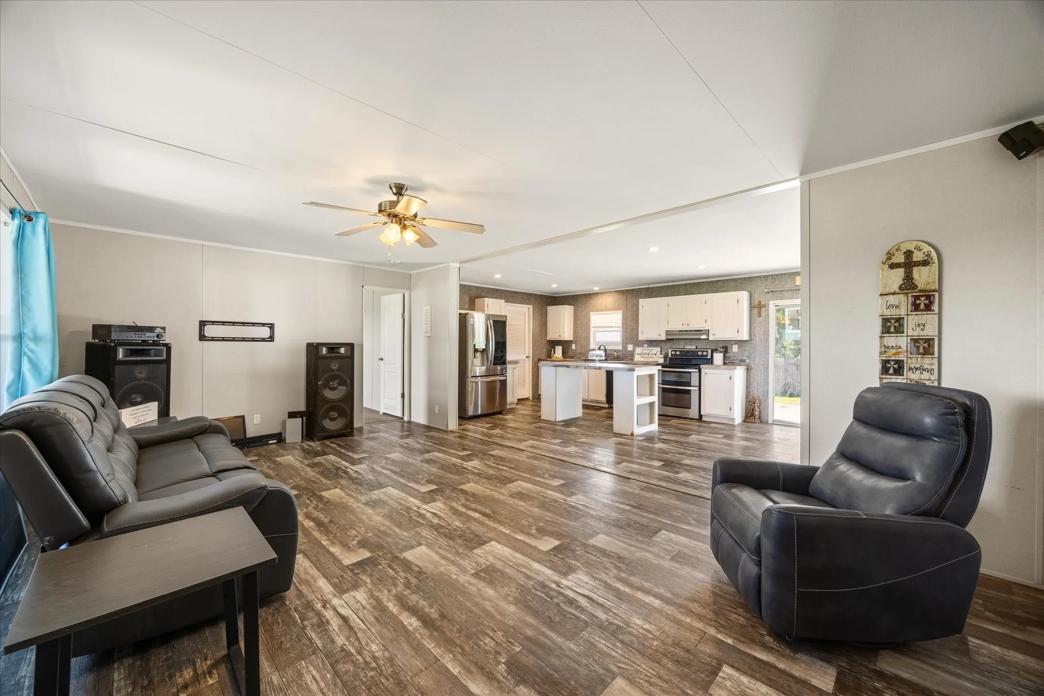 Open-concept living space featuring wood-finish flooring, a ceiling fan with integrated lighting, and a neutral color palette
