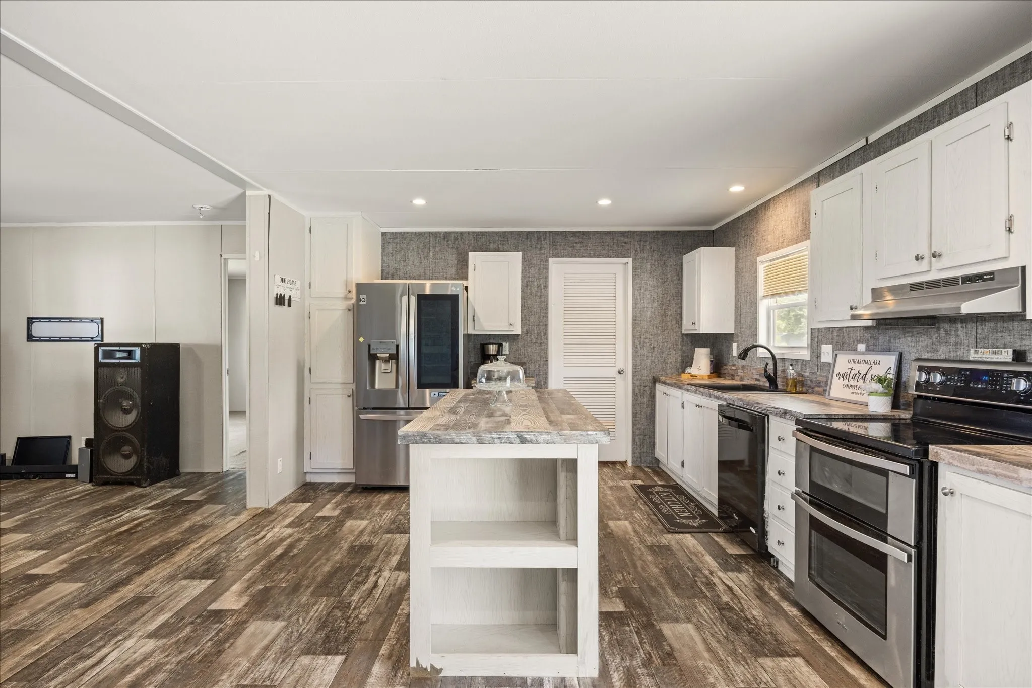 Modern kitchen featuring a central island, white cabinetry, stainless steel appliances, and wood-finish flooring
