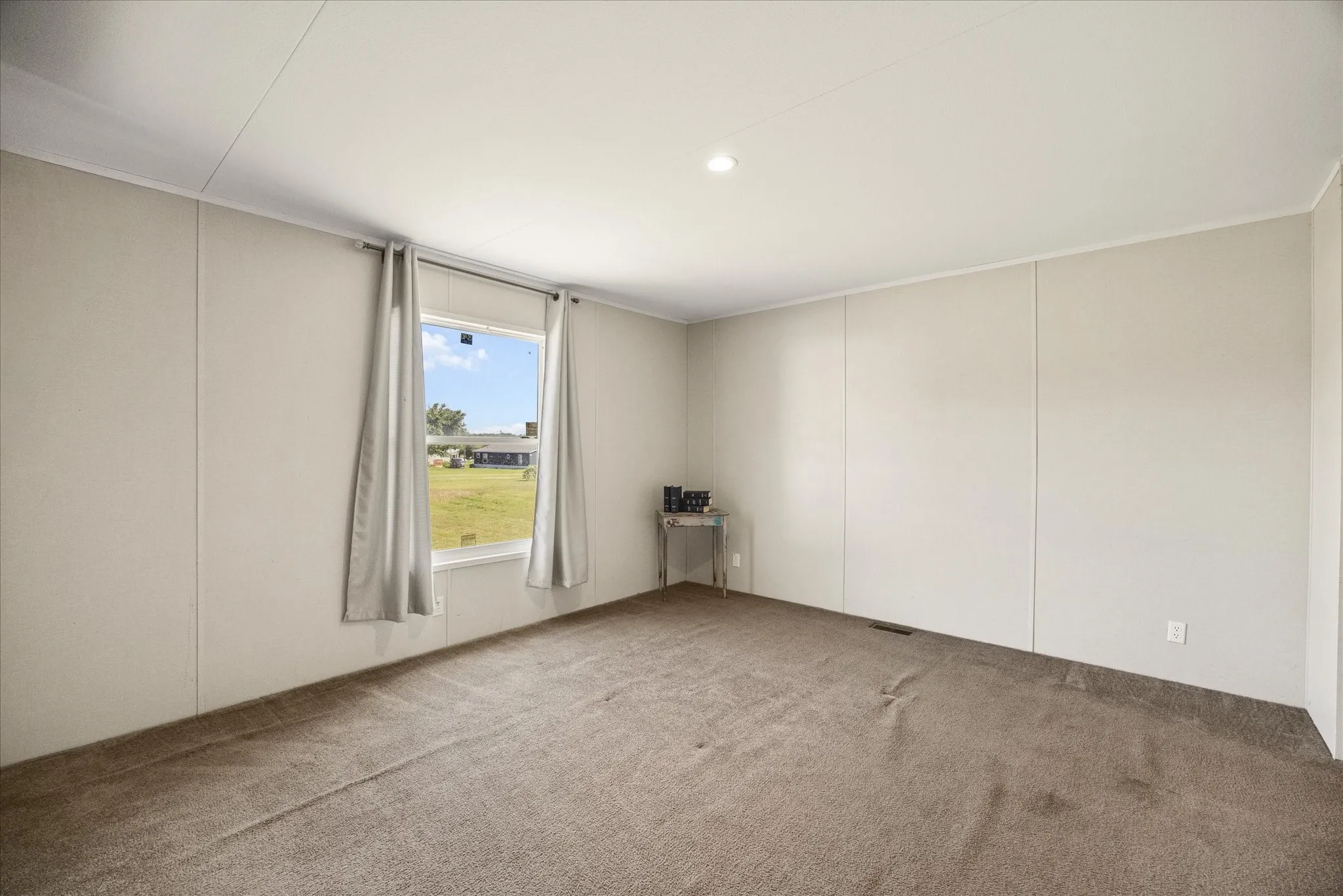 Spacious room featuring carpeting, neutral wall panels, and a prominent window