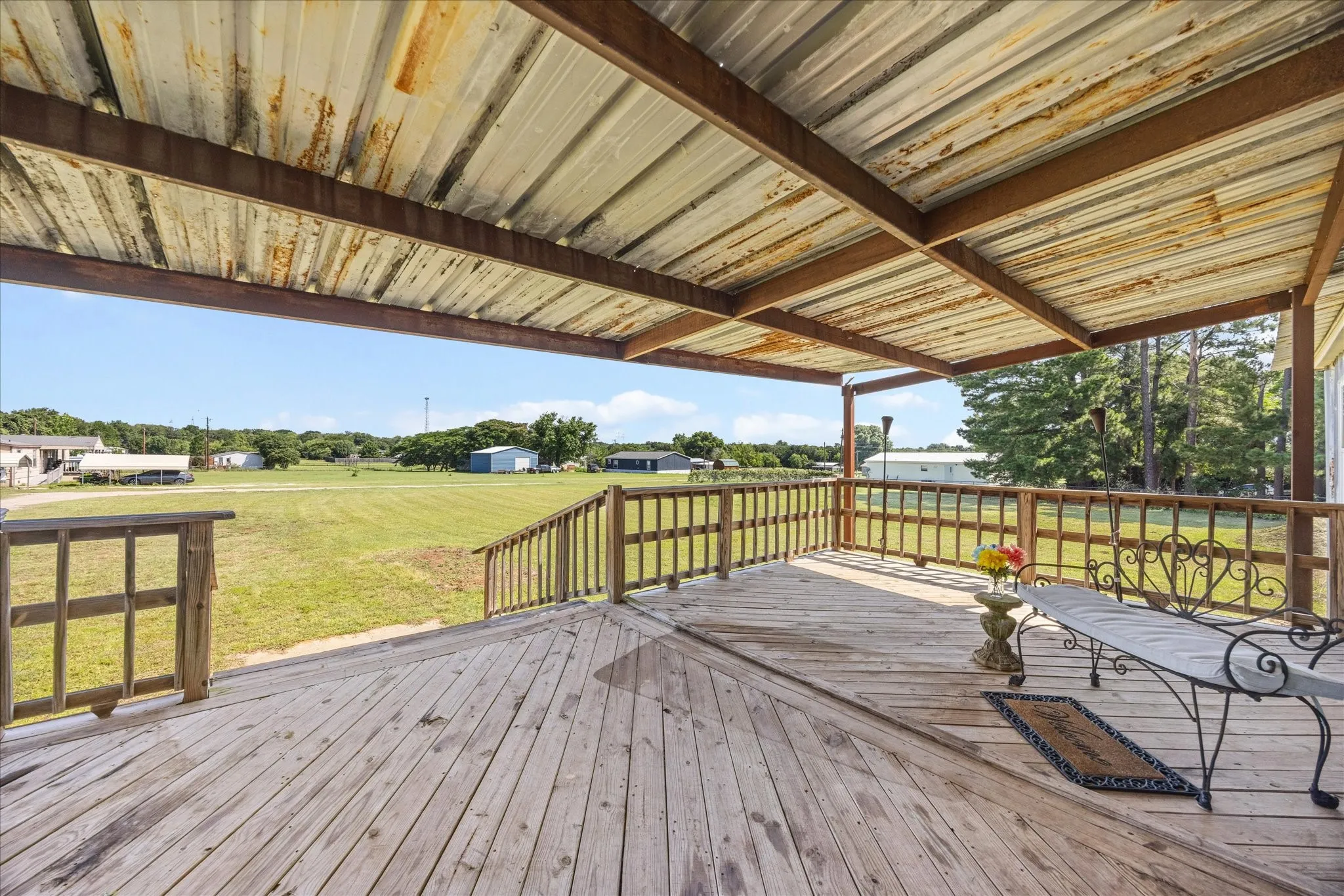 Expansive covered wooden deck featuring a metal roof structure, wooden railings, and a wide-open landscape