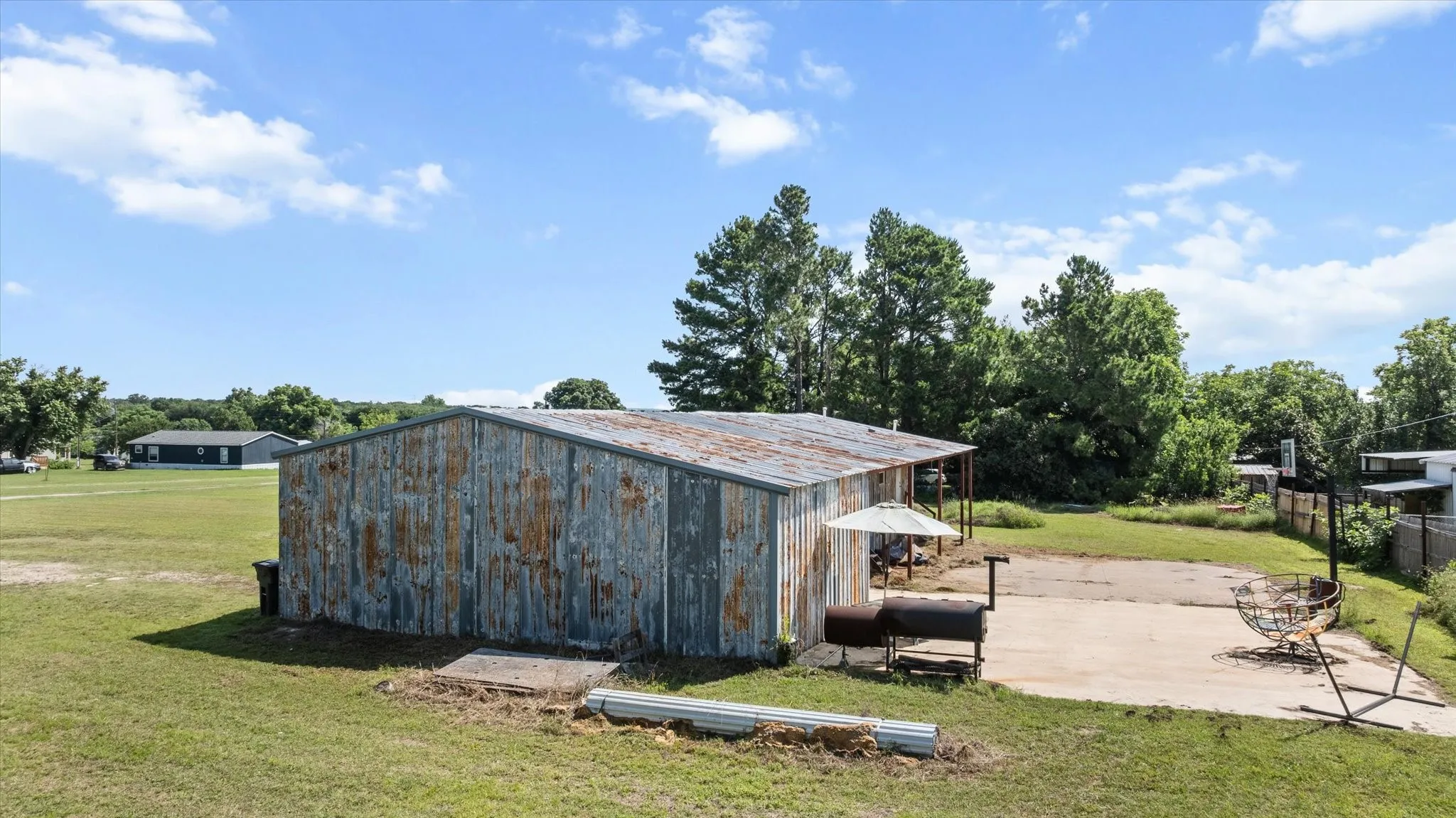 Metal outbuilding with a corrugated roof, concrete slab, and surrounding grassy area