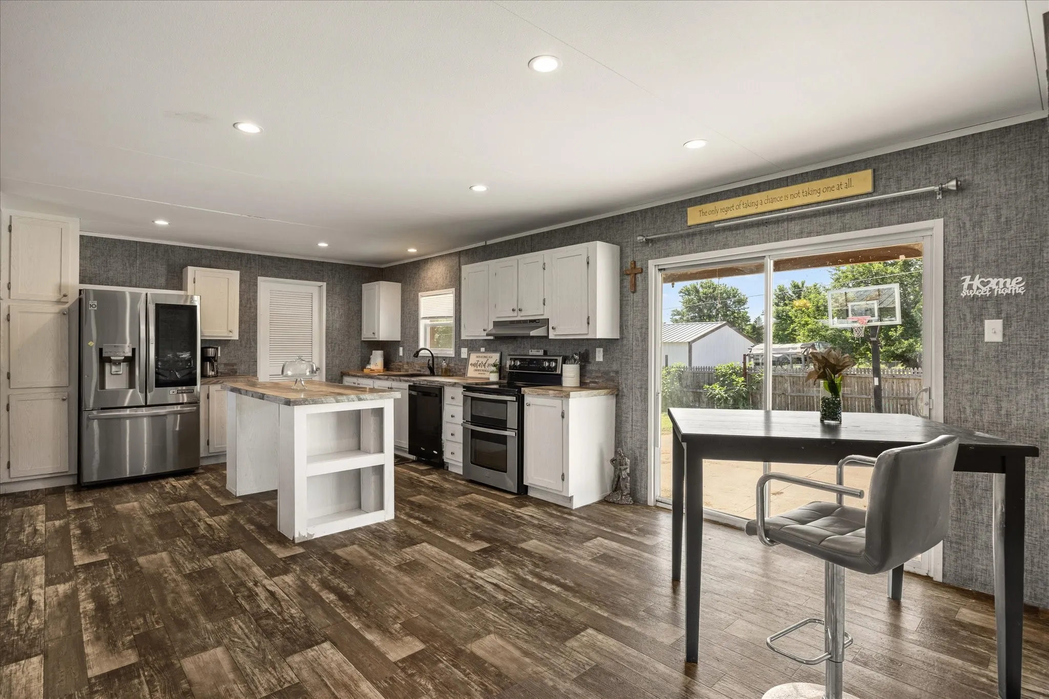 Open-concept kitchen featuring wood-finish flooring, white cabinetry, a central island with built-in shelving, stainless steel appliances, and a sliding glass door leading to the exterior