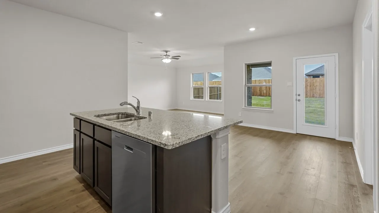 Kitchen island featuring a granite countertop, undermount stainless steel sink, and integrated dishwasher
