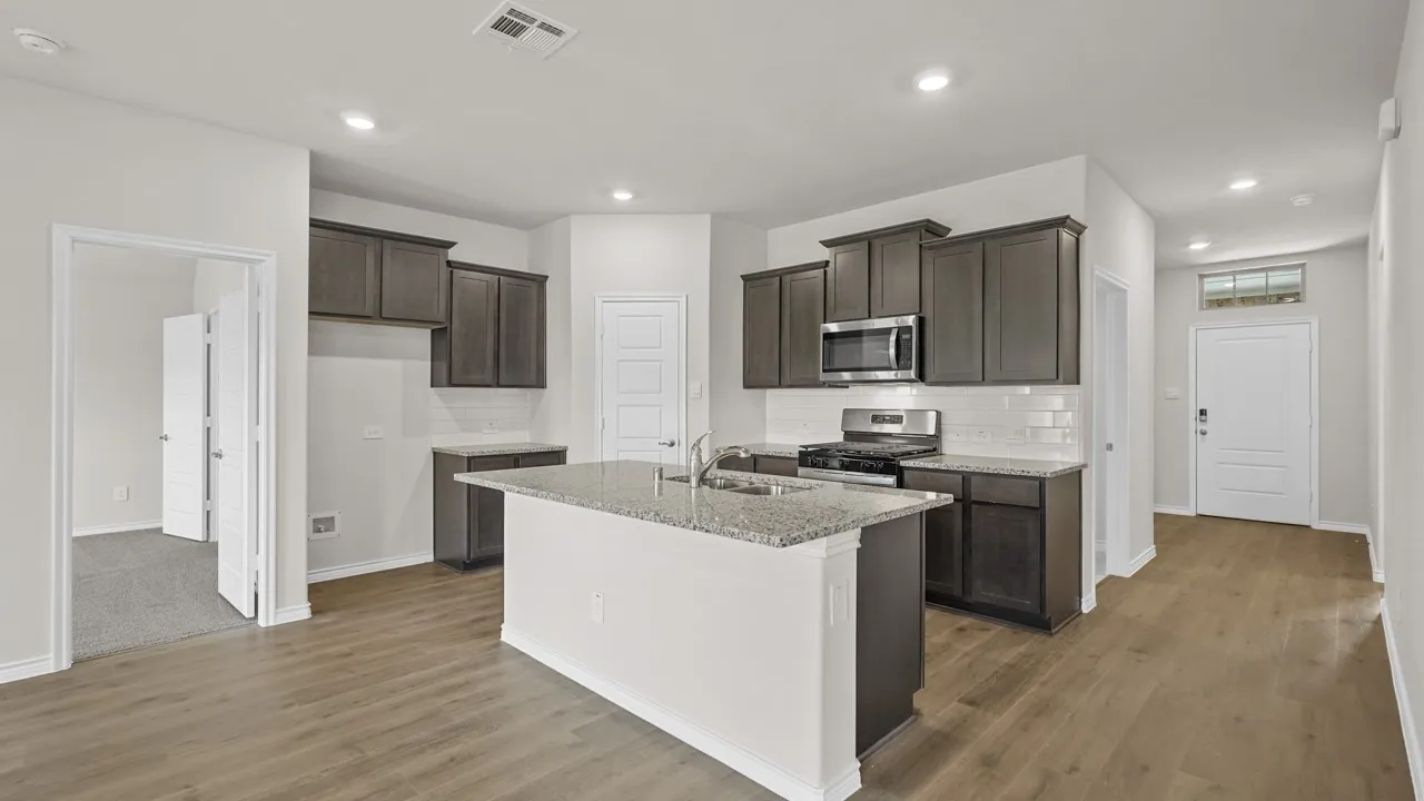 Open-concept kitchen featuring an island with a sink, granite countertops, wood-finish flooring, stainless steel appliances, and dark wood cabinetry