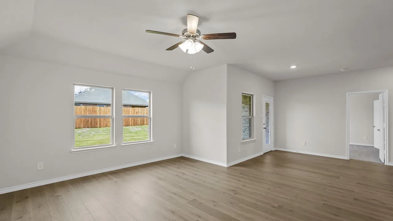 Spacious interior room featuring wood-finish flooring, vaulted ceiling, and a ceiling fan with light fixture