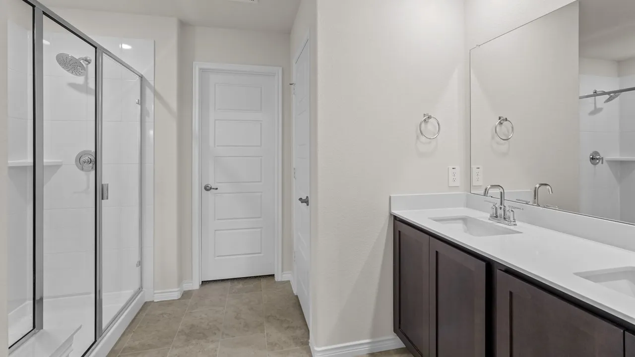 Bathroom featuring a glass-enclosed shower with a rainfall showerhead, a double vanity with a light-colored countertop, dark wood-finish cabinetry, and a large wall-mounted mirror