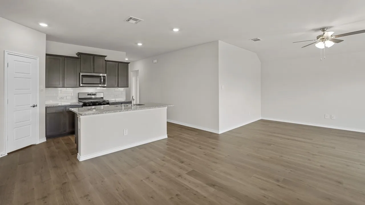 Open-concept living space featuring wood-finish flooring, a kitchen island with a granite-style countertop, stainless steel appliances, dark wood cabinetry, and recessed lighting