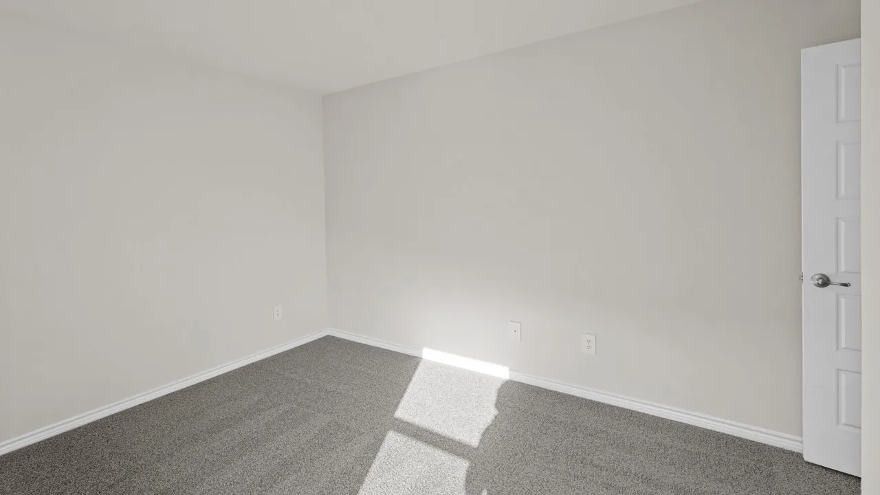 Neutral-toned room featuring light gray walls, dark gray carpet, white baseboards, and a paneled interior door with brushed nickel hardware