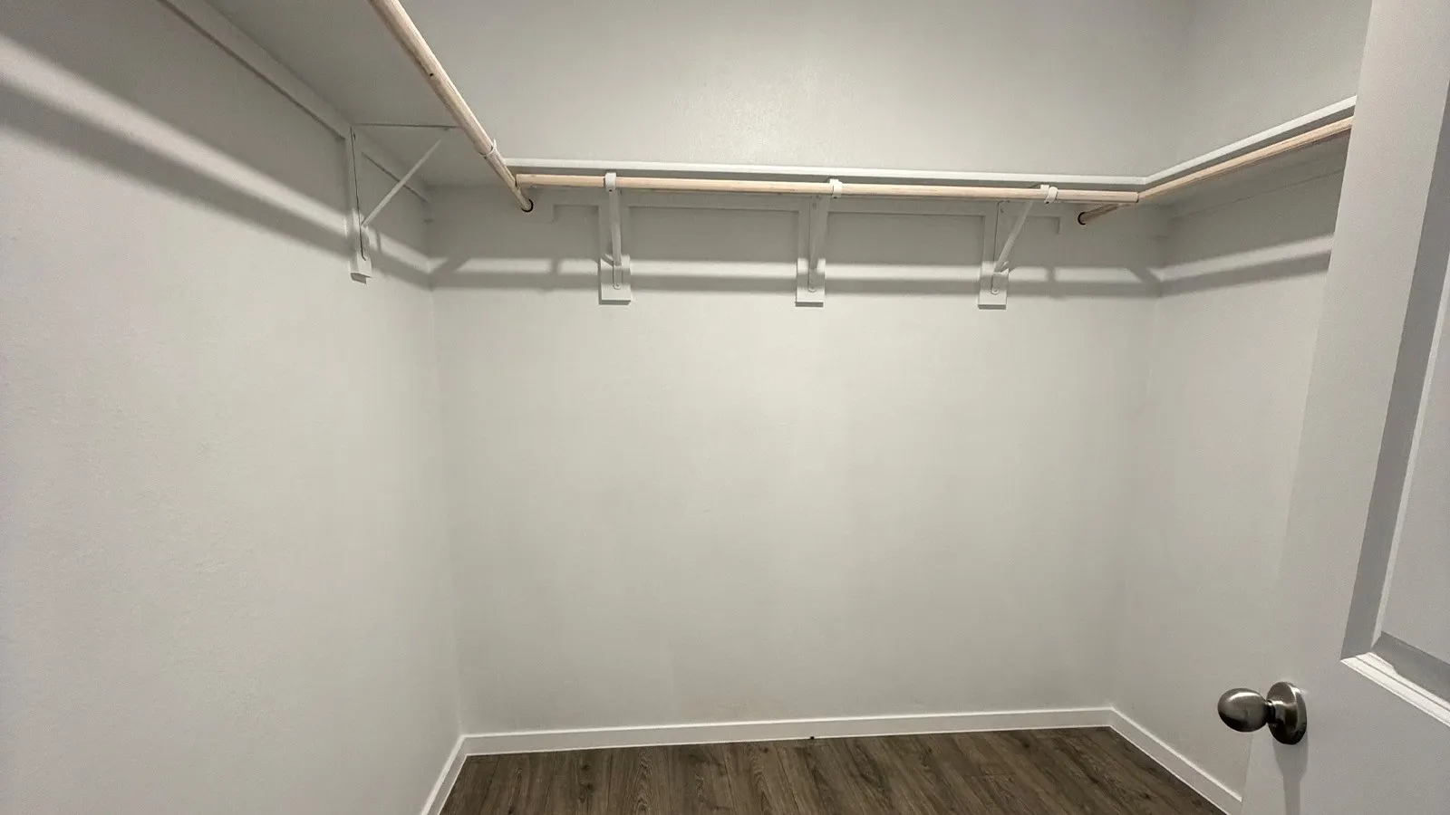 Walk-in closet featuring light gray walls, wood-finish flooring, and white trim