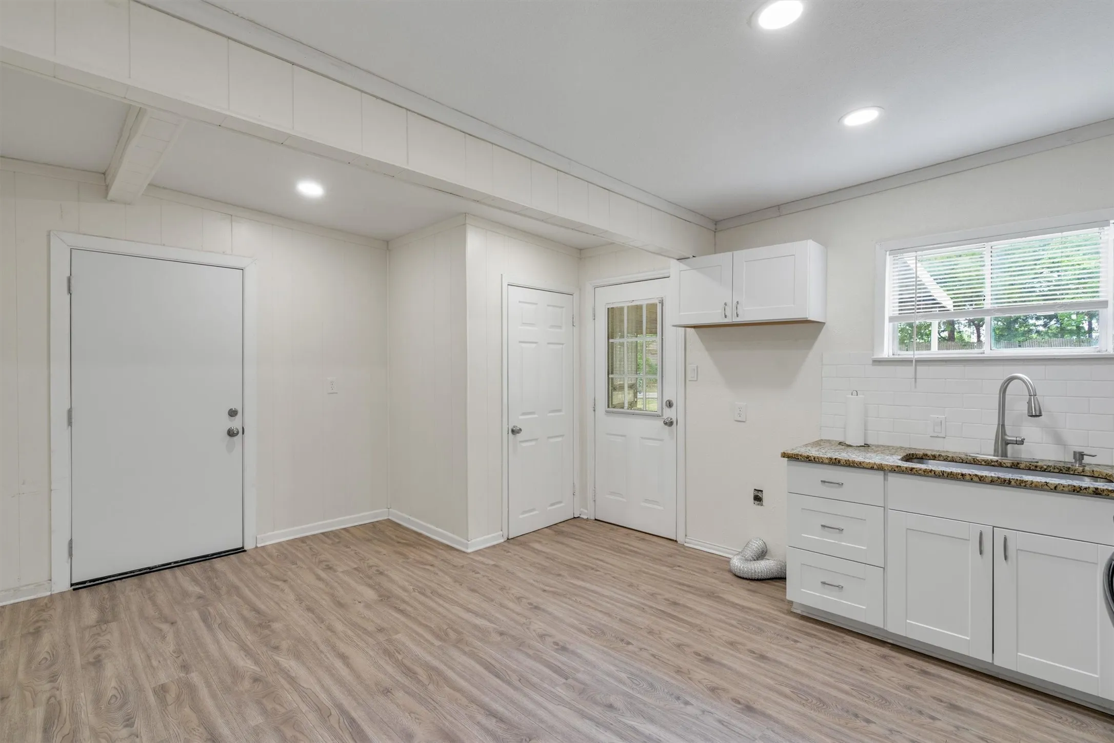 Kitchenette featuring white shaker-style cabinetry, granite-finish countertops, subway tile backsplash, and a stainless steel sink with a gooseneck faucet