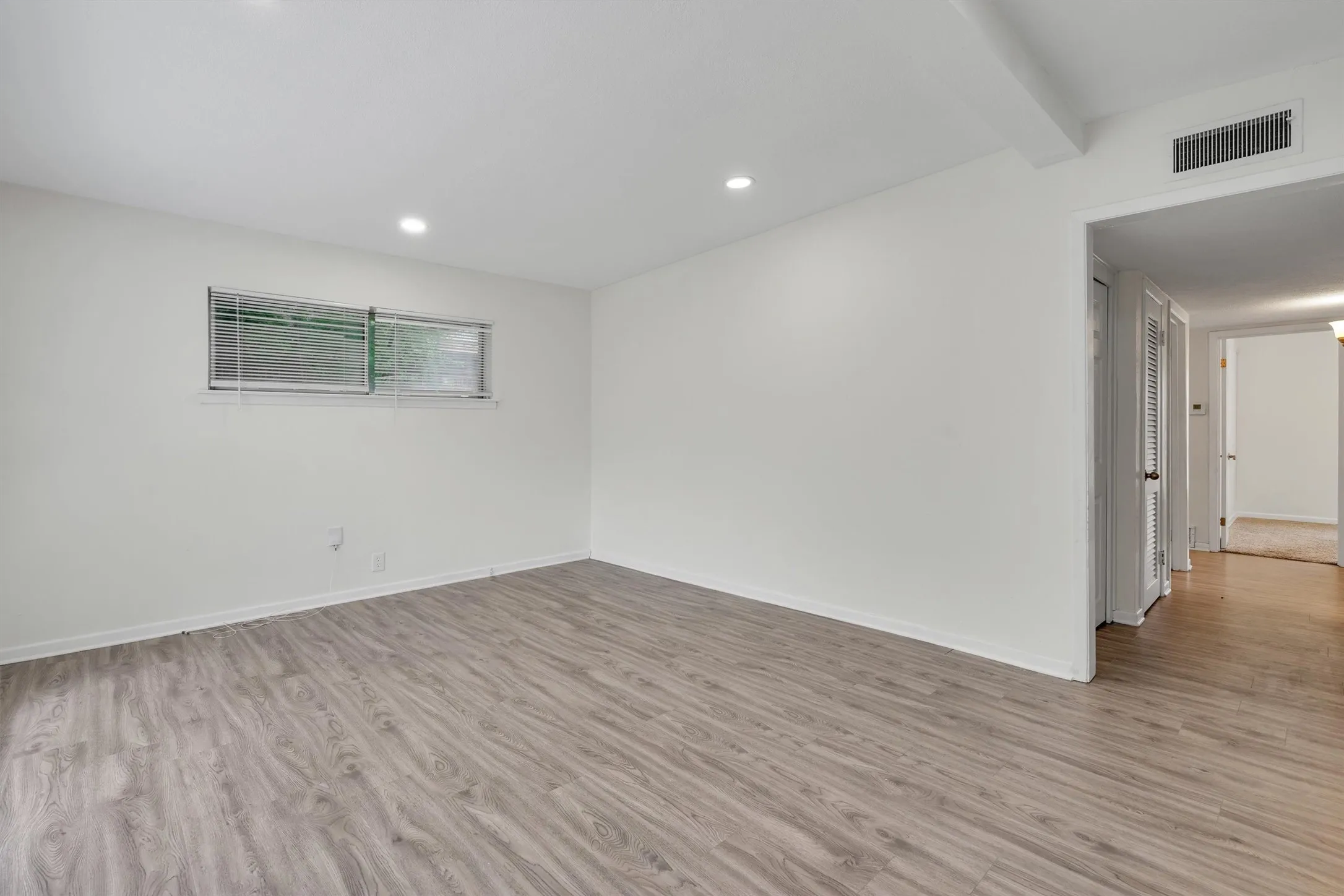 Spacious room featuring wood-finish flooring, recessed lighting, and white walls