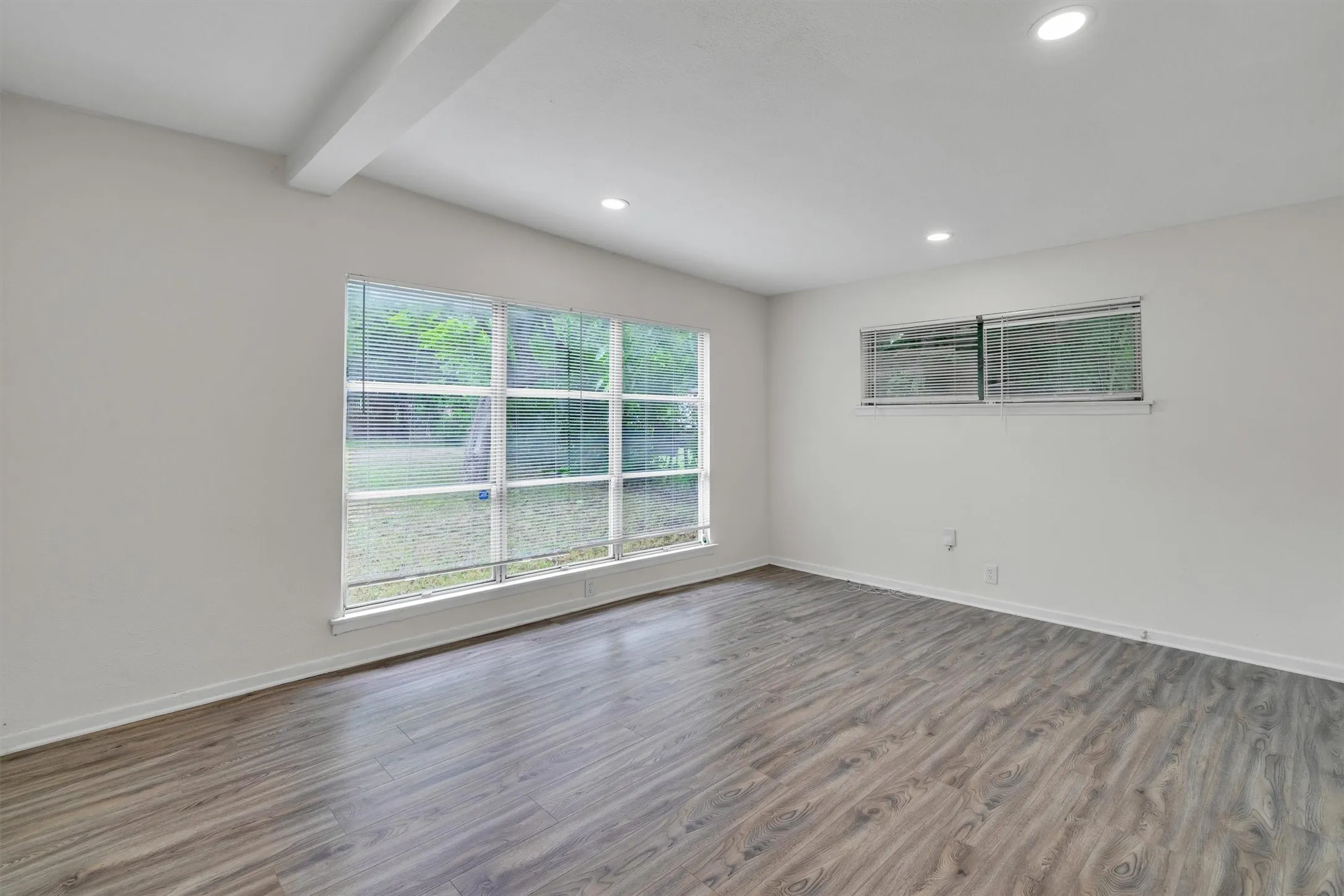 Spacious room featuring wood-finish flooring, recessed lighting, and a large picture window