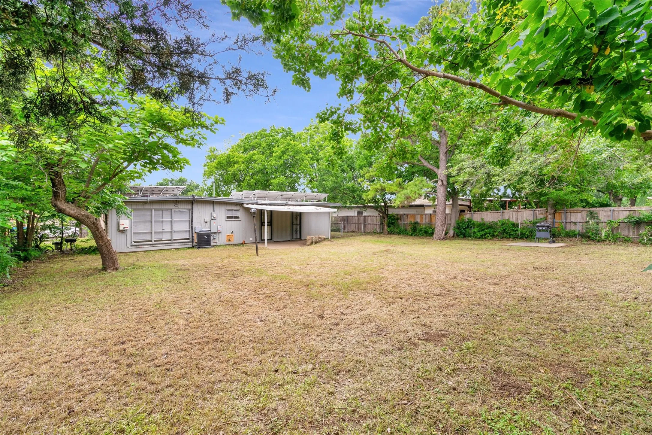 Expansive backyard featuring a large grass area, mature trees, and a privacy fence