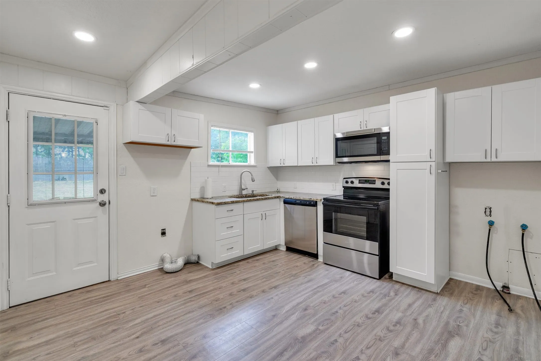 Modern kitchen featuring white shaker cabinetry, stainless steel appliances, light-toned wood-finish flooring, recessed lighting, and a white subway tile backsplash