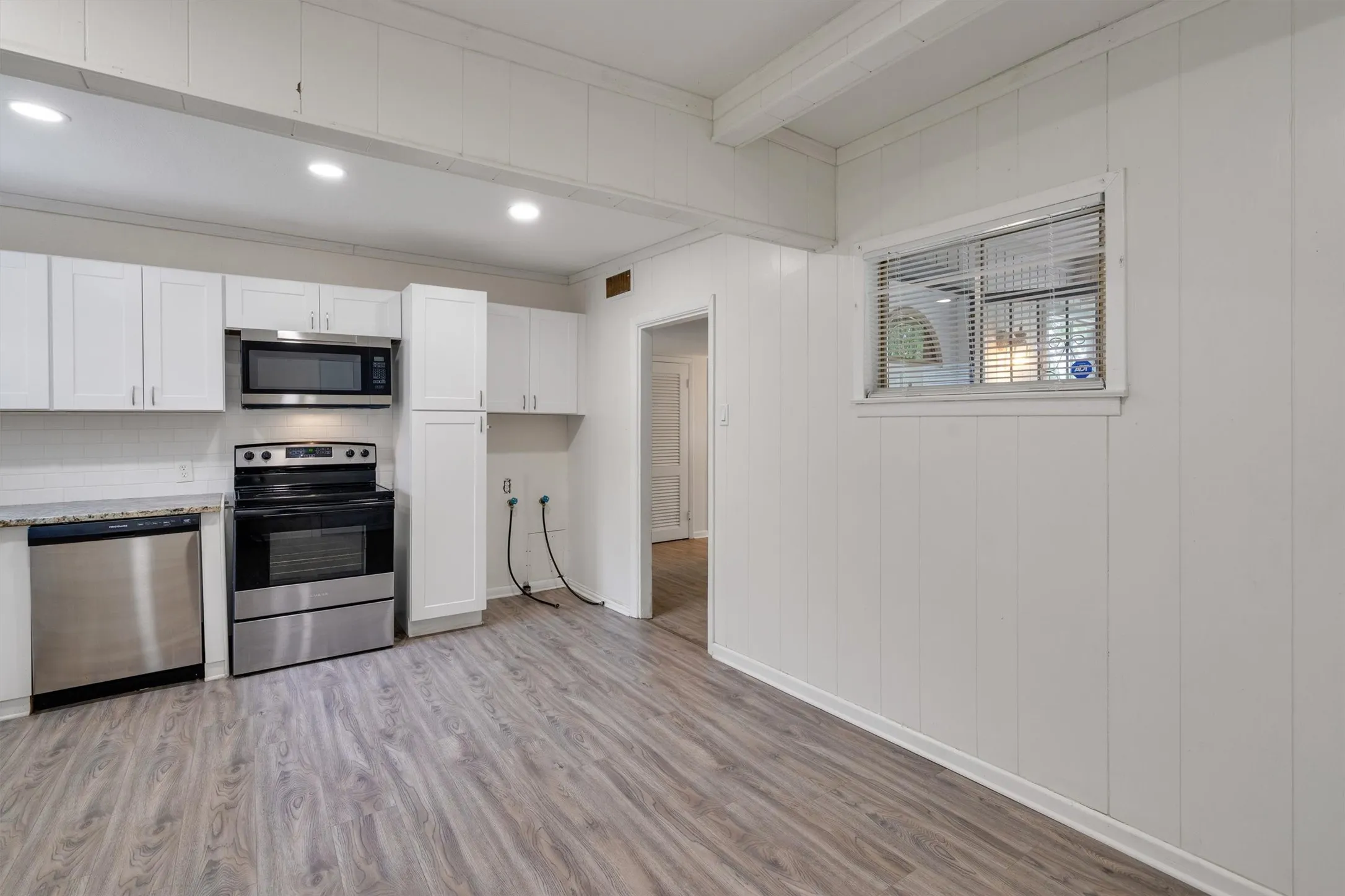 Kitchen featuring stainless steel appliances, white cabinetry, laminate countertops, and wood-finish flooring