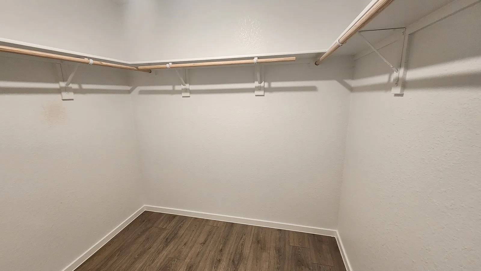 Spacious walk-in closet featuring wood-finish flooring, white baseboards, and built-in shelving with hanging rods
